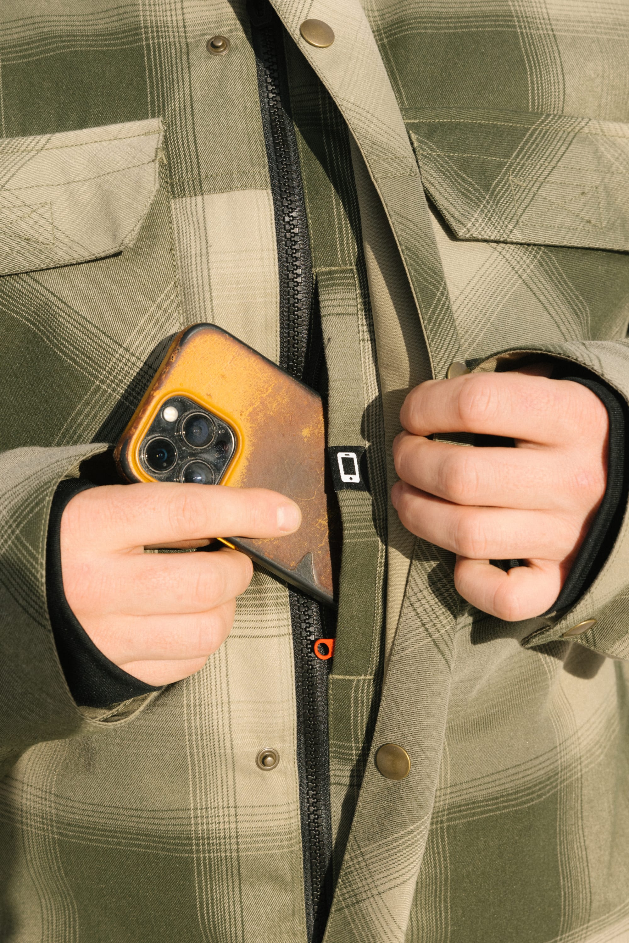 A person wearing the 686 Men's Woodland™ Insulated Jacket holds a phone with a yellow case while partially zipping up the jacket, both hands visible.