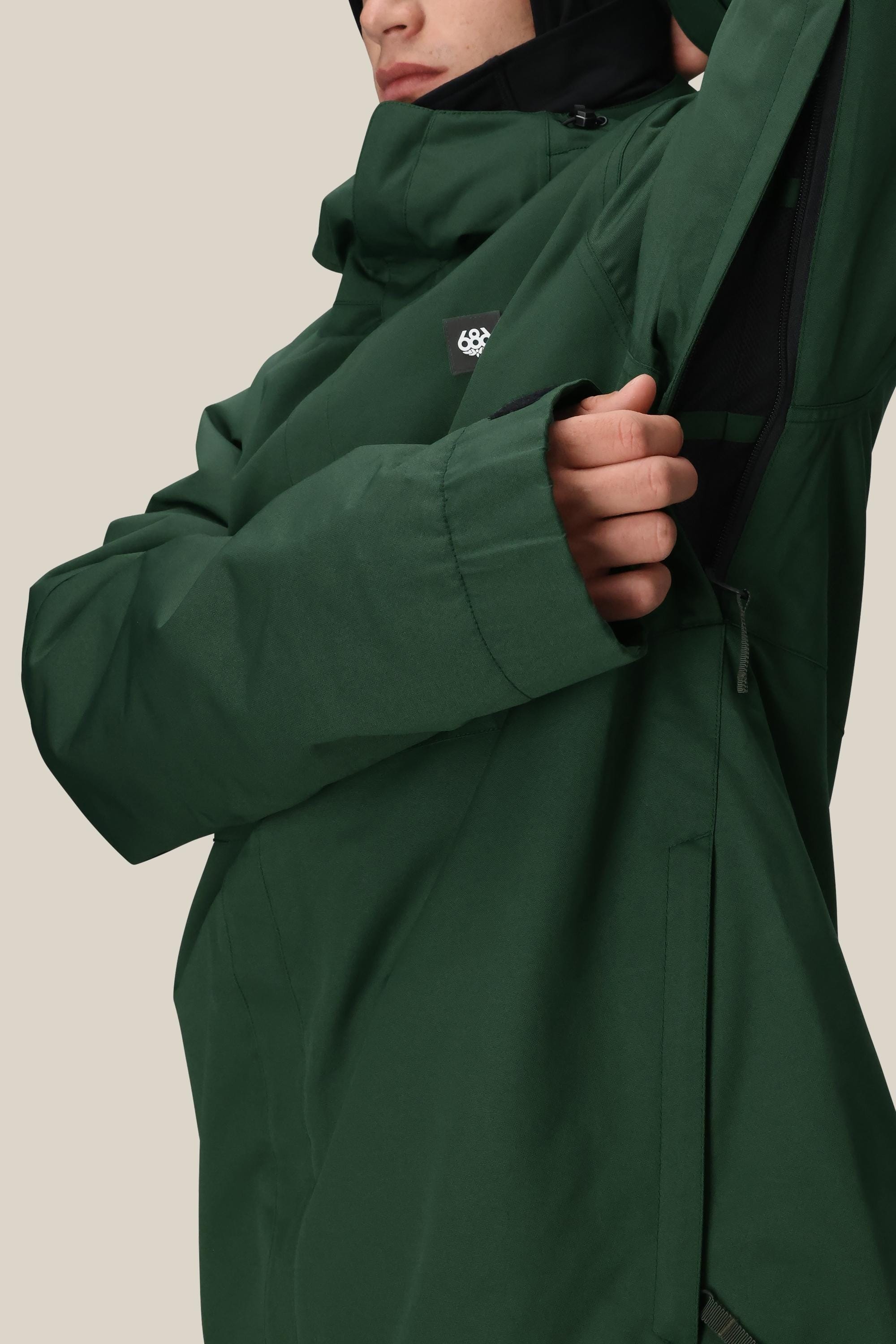 Person wearing a 686 Men's Foundation™ Insulated Jacket in green, unzipping an underarm vent. Their face is partially visible against a plain beige background.