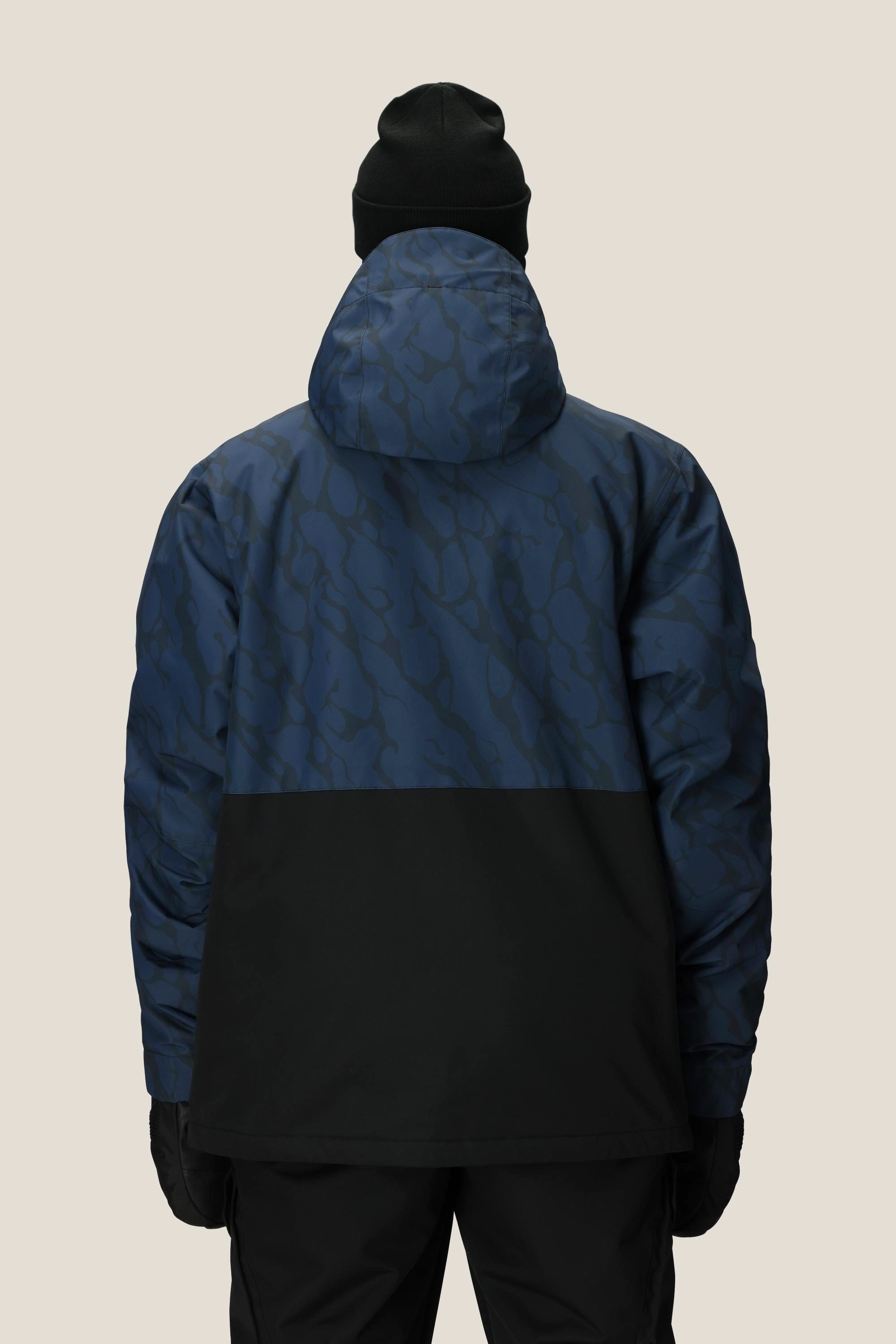A person is shown from the back against a plain light background, wearing black pants, a black beanie, black gloves, and the 686 Men's Foundation™ Insulated Jacket by 686 in blue and black with a subtle pattern.