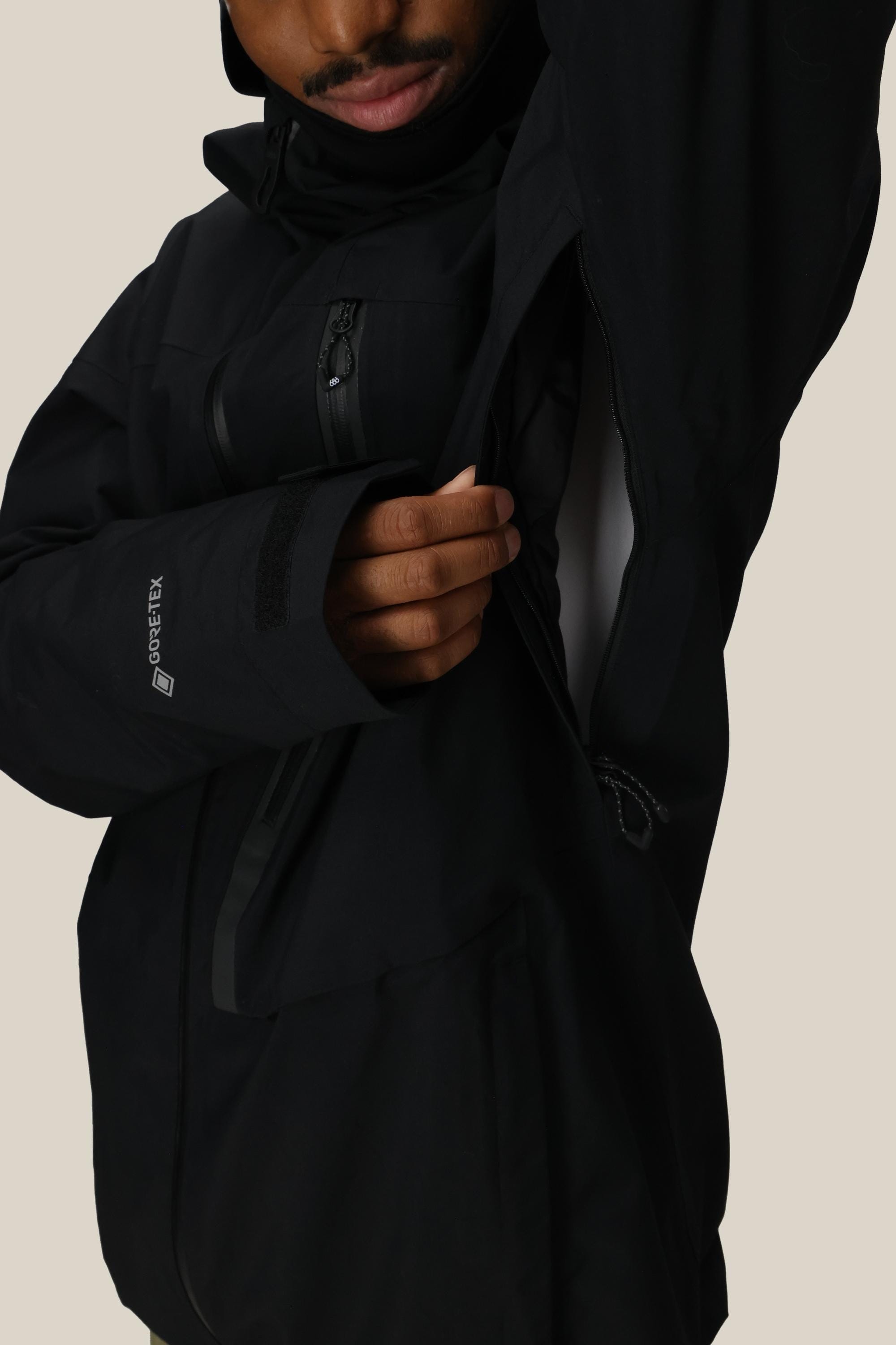 A person in the 686 Men's GORE-TEX GT Thermagraph® Jacket by 686 unzips the underarm vent, showing a white inner layer. Their face is partly visible, with a plain beige background.