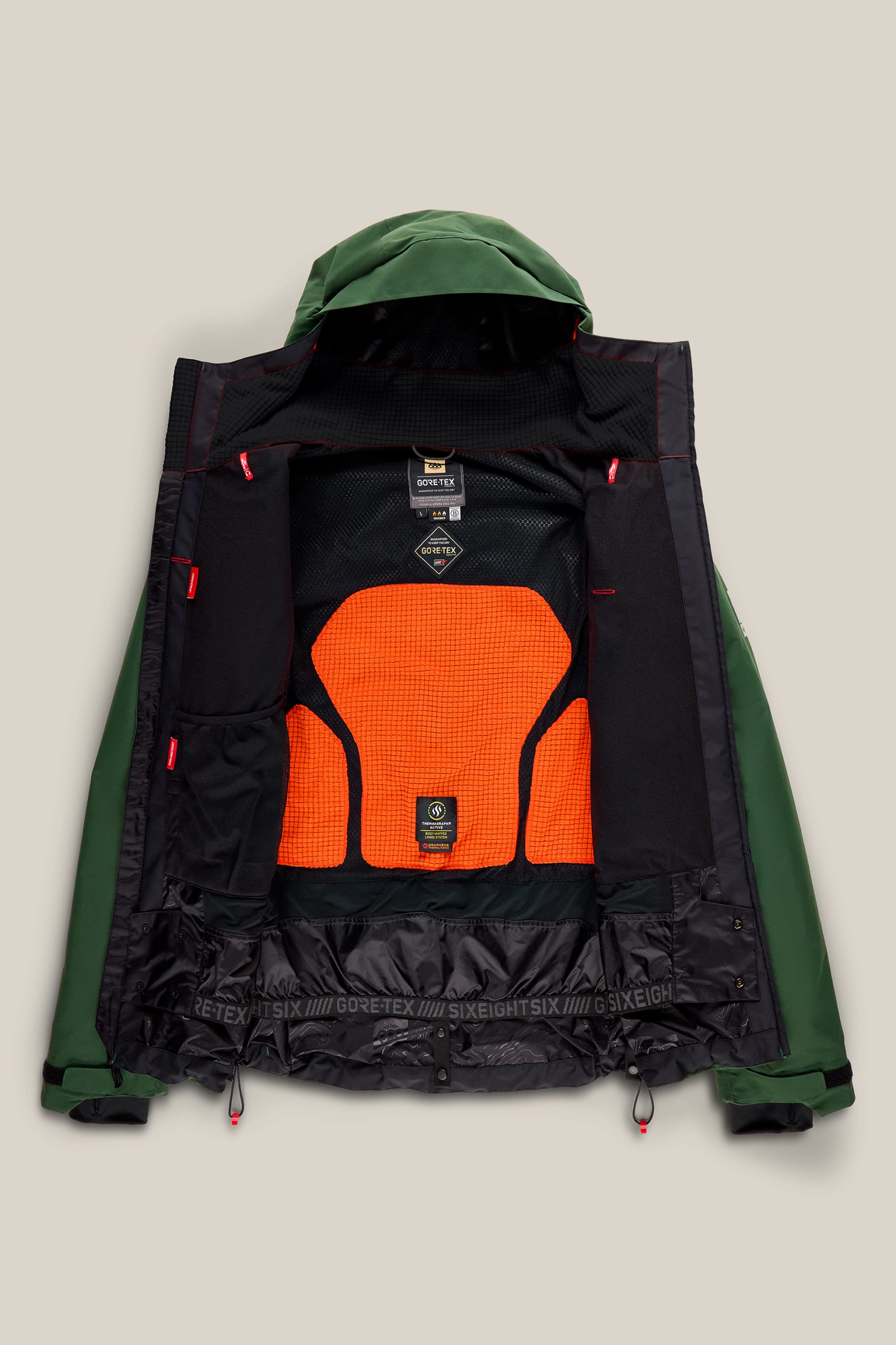 The 686 Men’s GORE-TEX® GT Thermagraph® Jacket by 686 features a front-open design in green, revealing a bright orange and black mesh interior lining, black trim, various interior tags, a hood, and red accents along the inner seams.