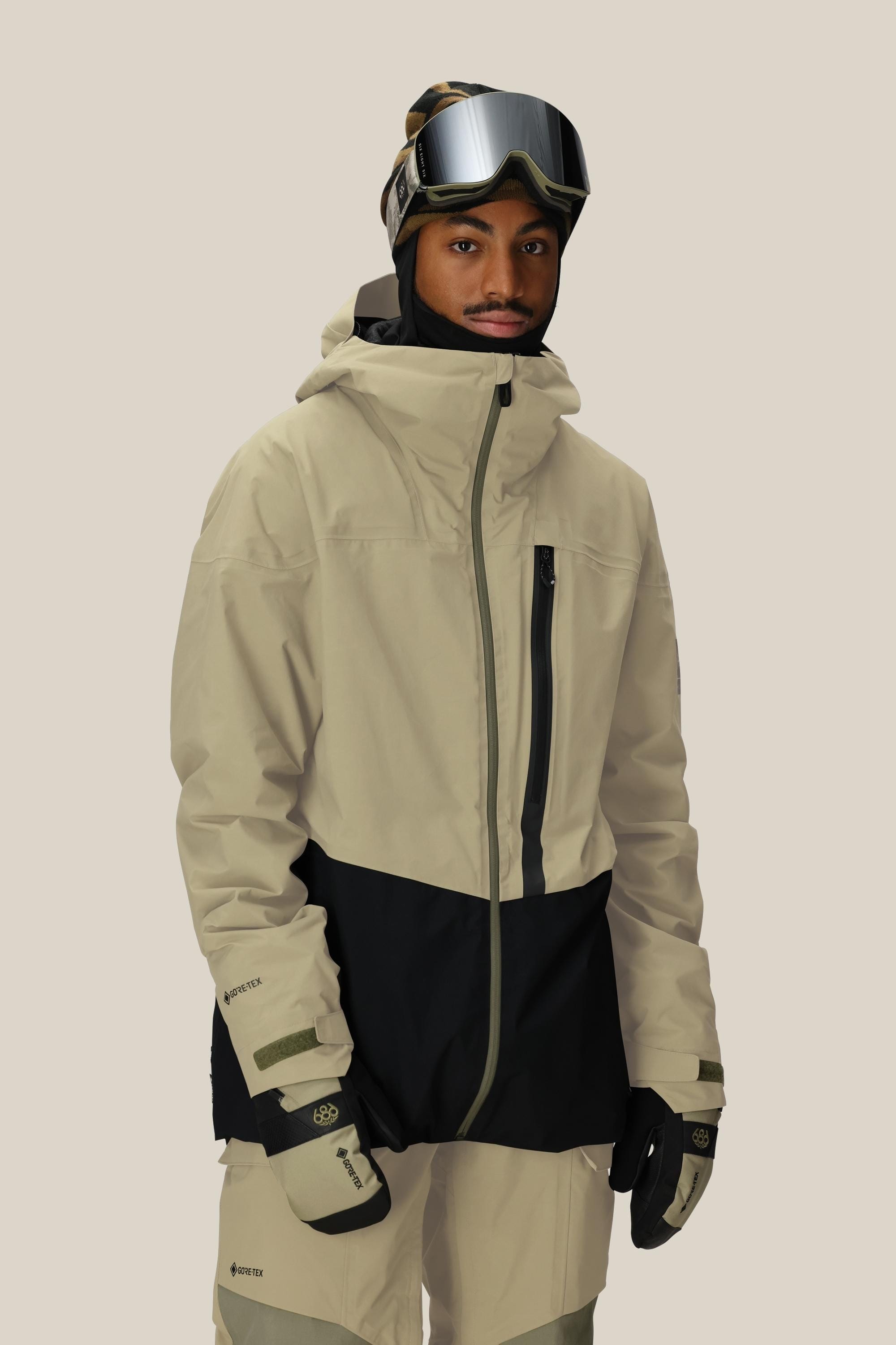 A person wearing the 686 Men's GORE-TEX GT Thermagraph® Jacket in beige and black stands against a plain background, looking at the camera.