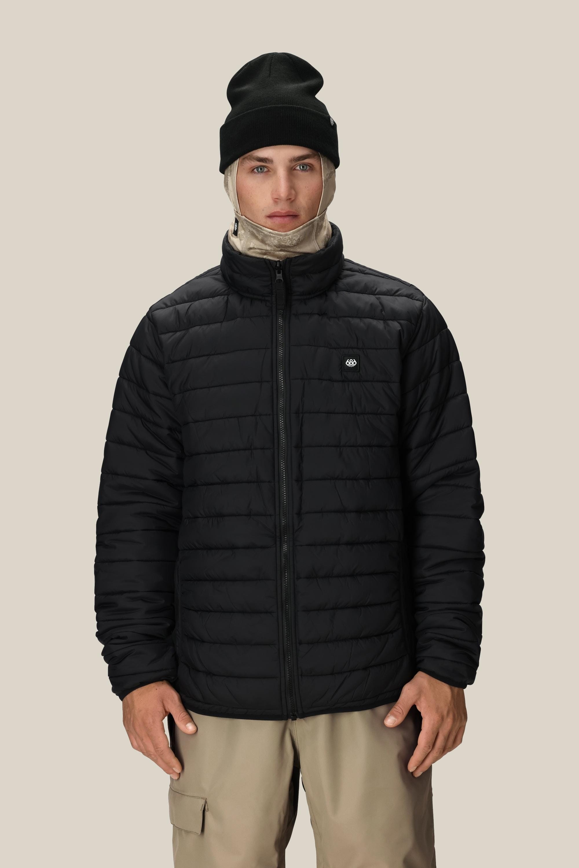 A person wearing the 686 Men's SMARTY® 3-In-1 Form Jacket in black, beige pants, a black beanie, and a beige neck gaiter stands facing forward against a plain beige background.