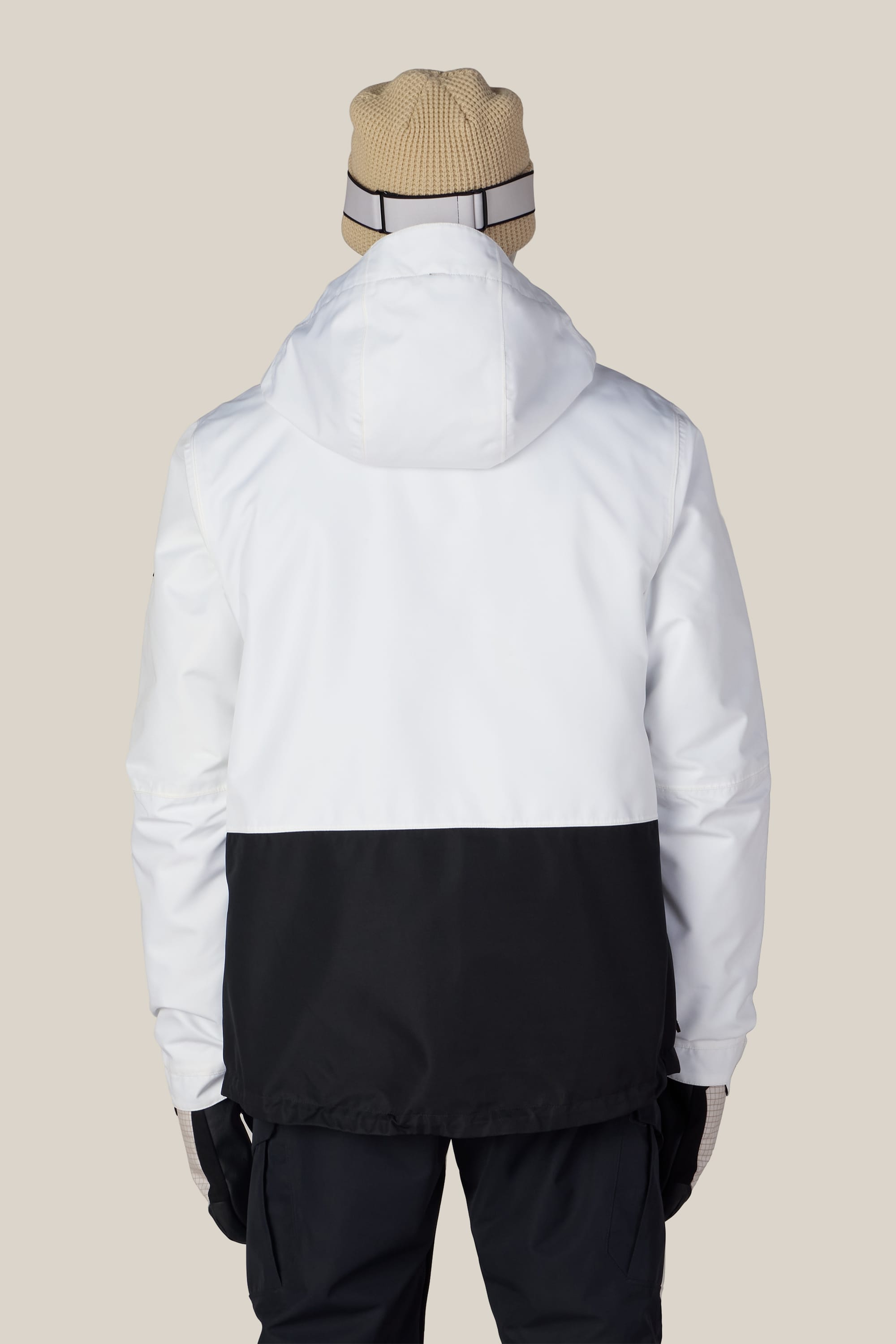 A person stands with their back to the camera against a plain beige background, wearing a beige beanie, black pants, gloves, and the 686 Men’s SMARTY® 3-In-1 Form Jacket by 686—a white and black hooded jacket.