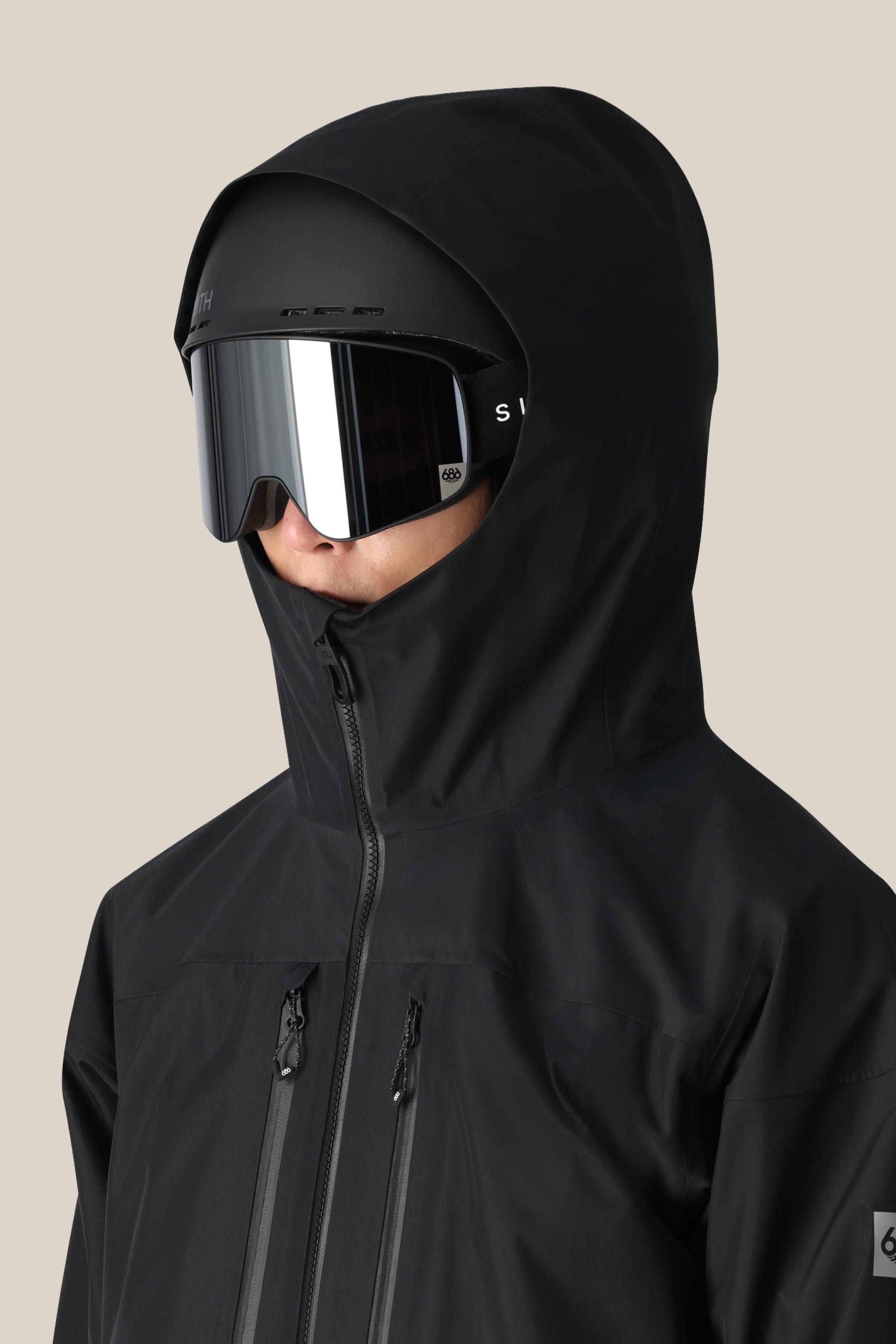 A person wearing the 686 Men's GORE-TEX 3L ATV Thermagraph® Jacket with the hood up and large, reflective ski goggles faces slightly right against a plain beige background.