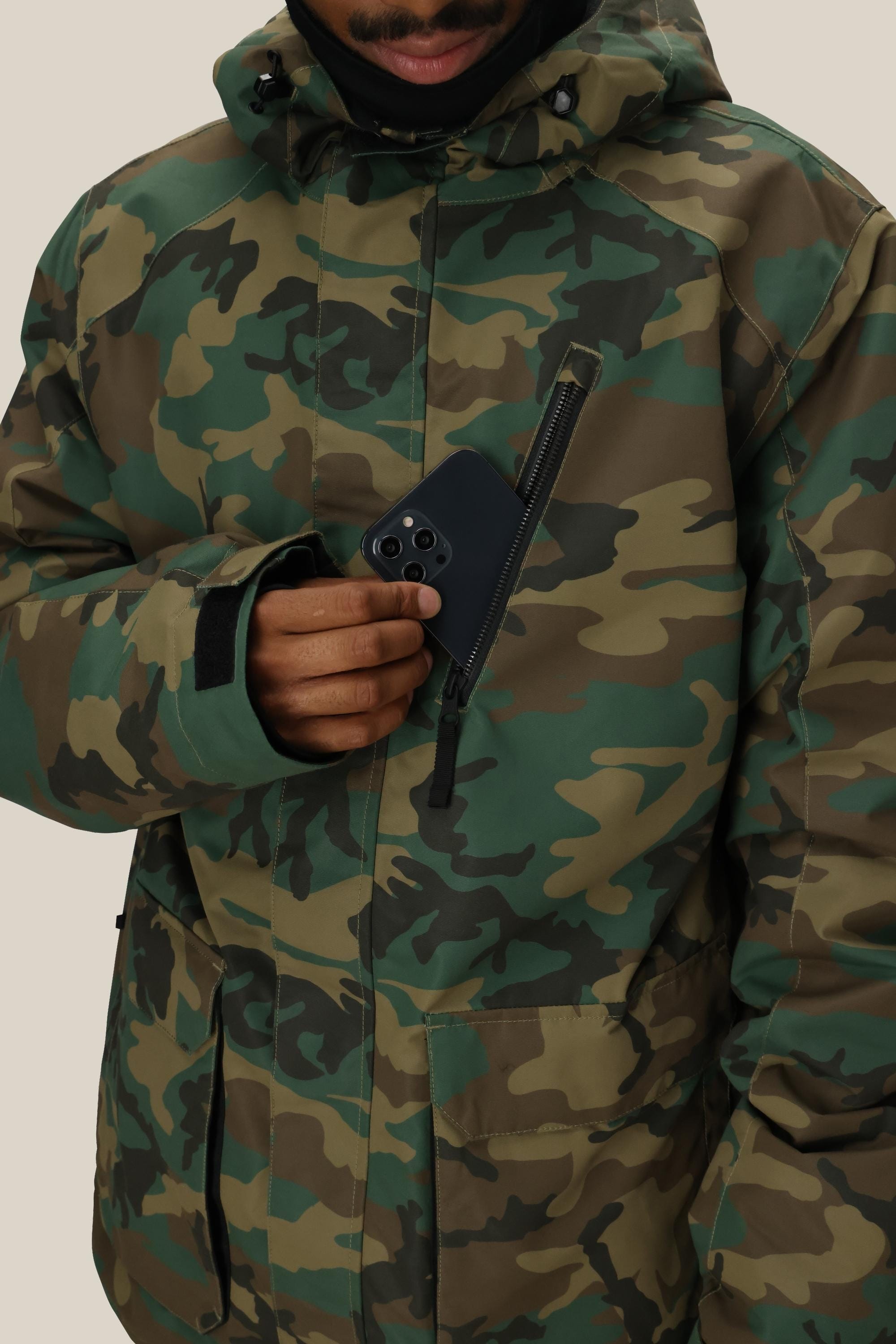 A person in a 686 Men's Nightline™ Insulated Jacket puts a black smartphone into the zippered chest pocket. Only part of their face is visible, set against a plain, light-colored background.