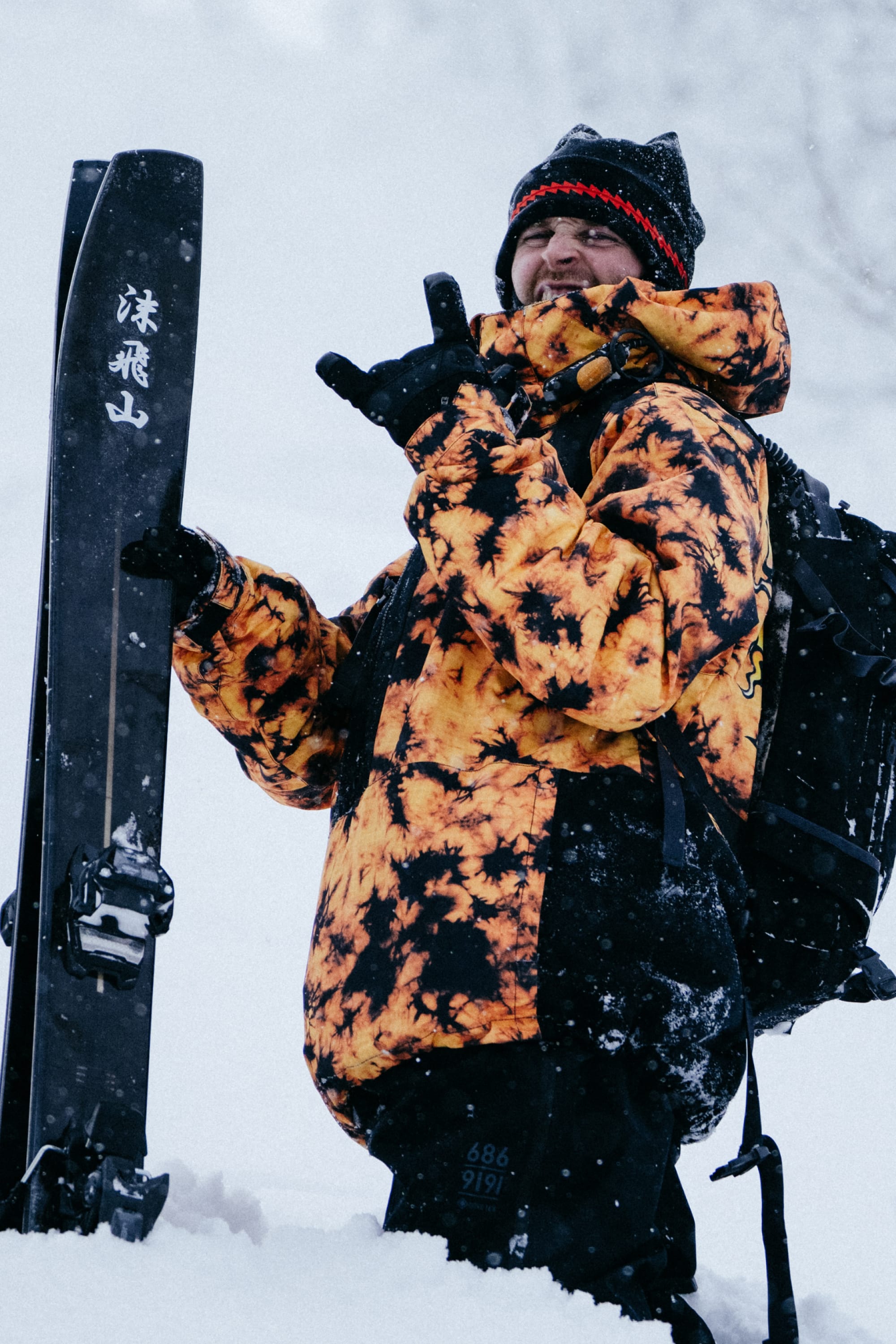 Wearing the 686 Mens Sublime Shell Anorak, a man in deep snow holds skis and gestures happily, smiling in his waterproof jacket by 686 on a snowy day.