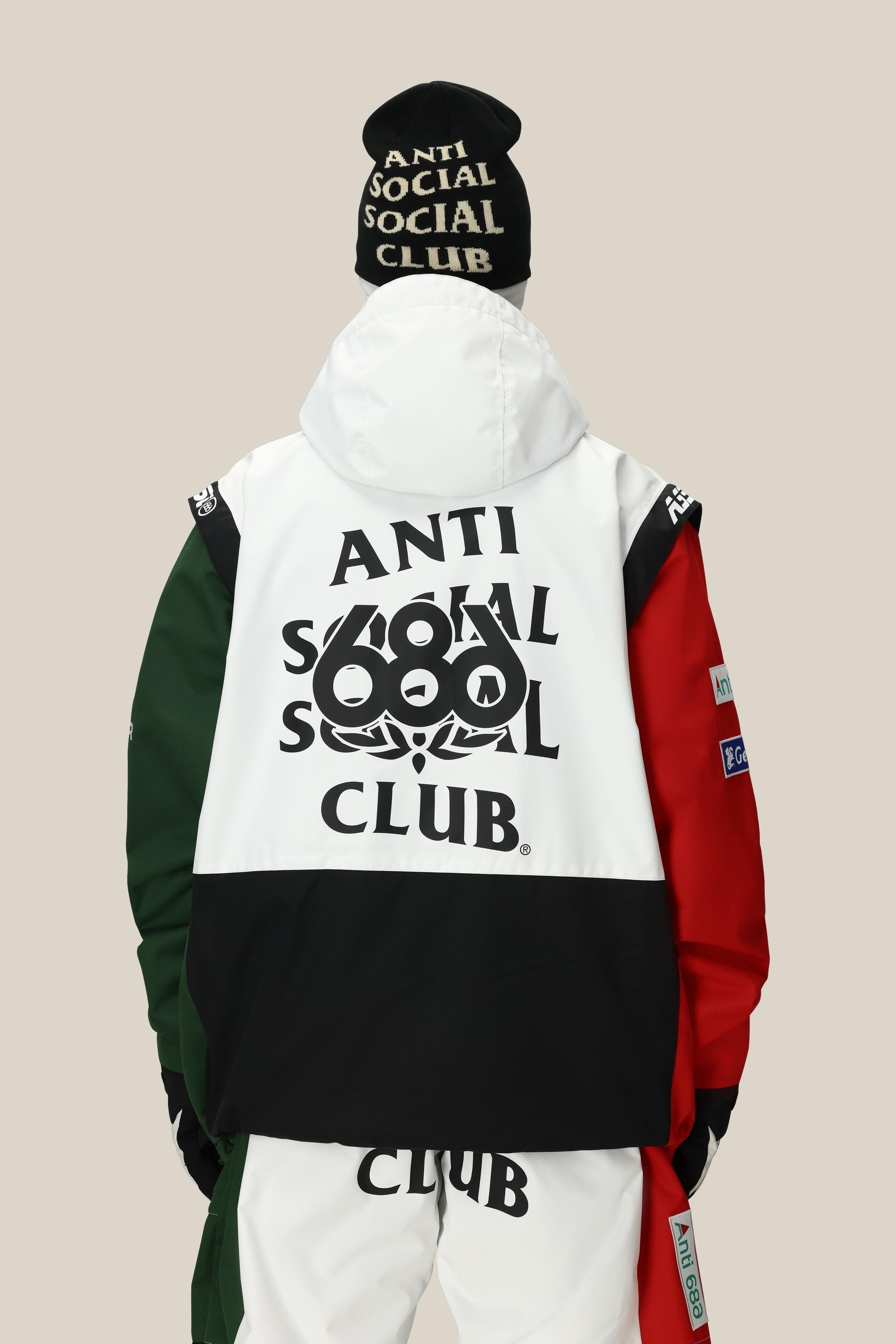 A person faces away, wearing the 686 Mens ASSC F1 Shell Anorak in white, black, red, and green with bold ANTI SOCIAL SOCIAL CLUB text on the back. They also wear a matching beanie and white pants with the same branding.