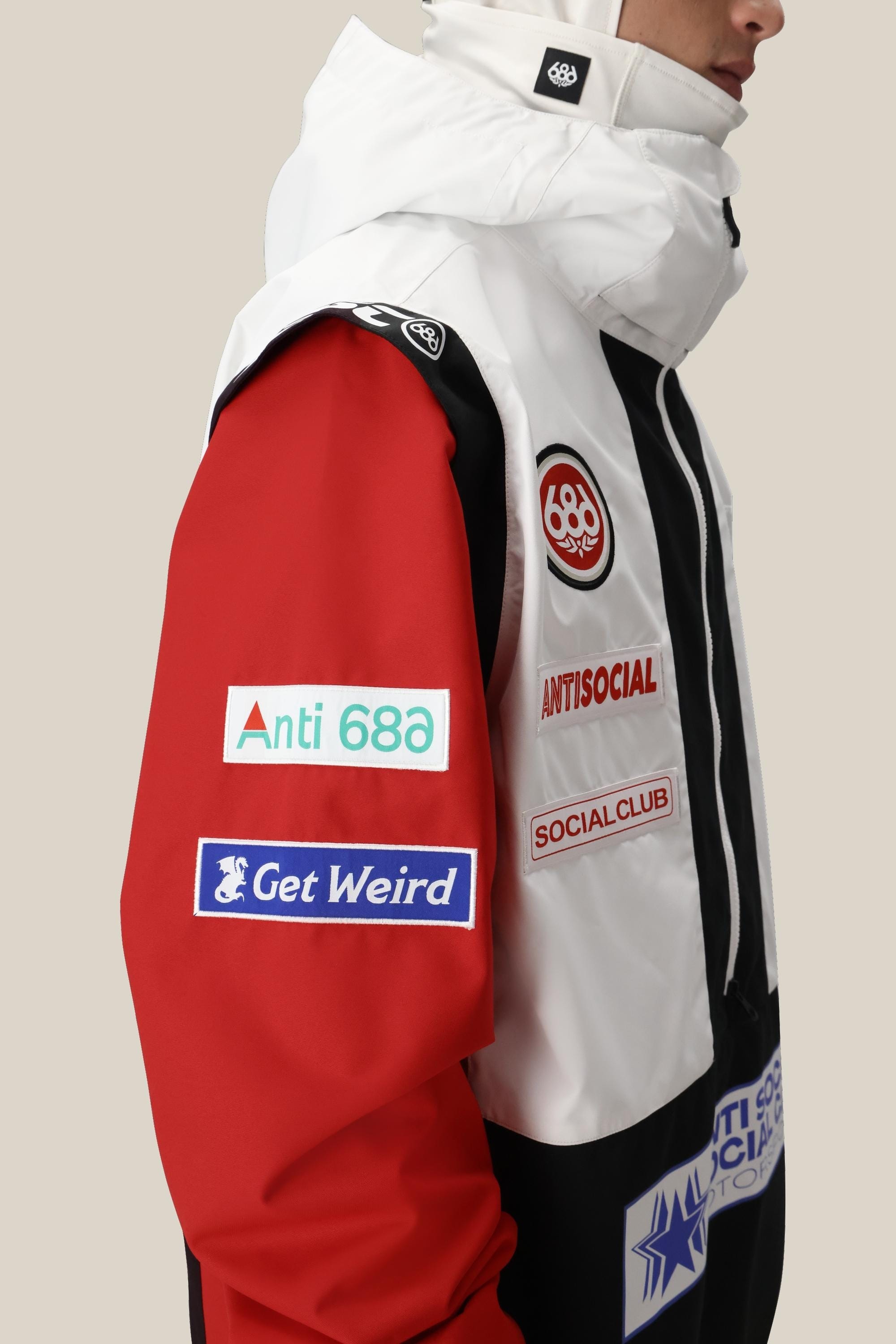 A person wears the 686 Mens ASSC F1 Shell Anorak in white, black, and red, featuring Anti 68a, ANTISOCIAL SOCIAL CLUB, and Get Weird patches on the sleeve and chest against a plain background.