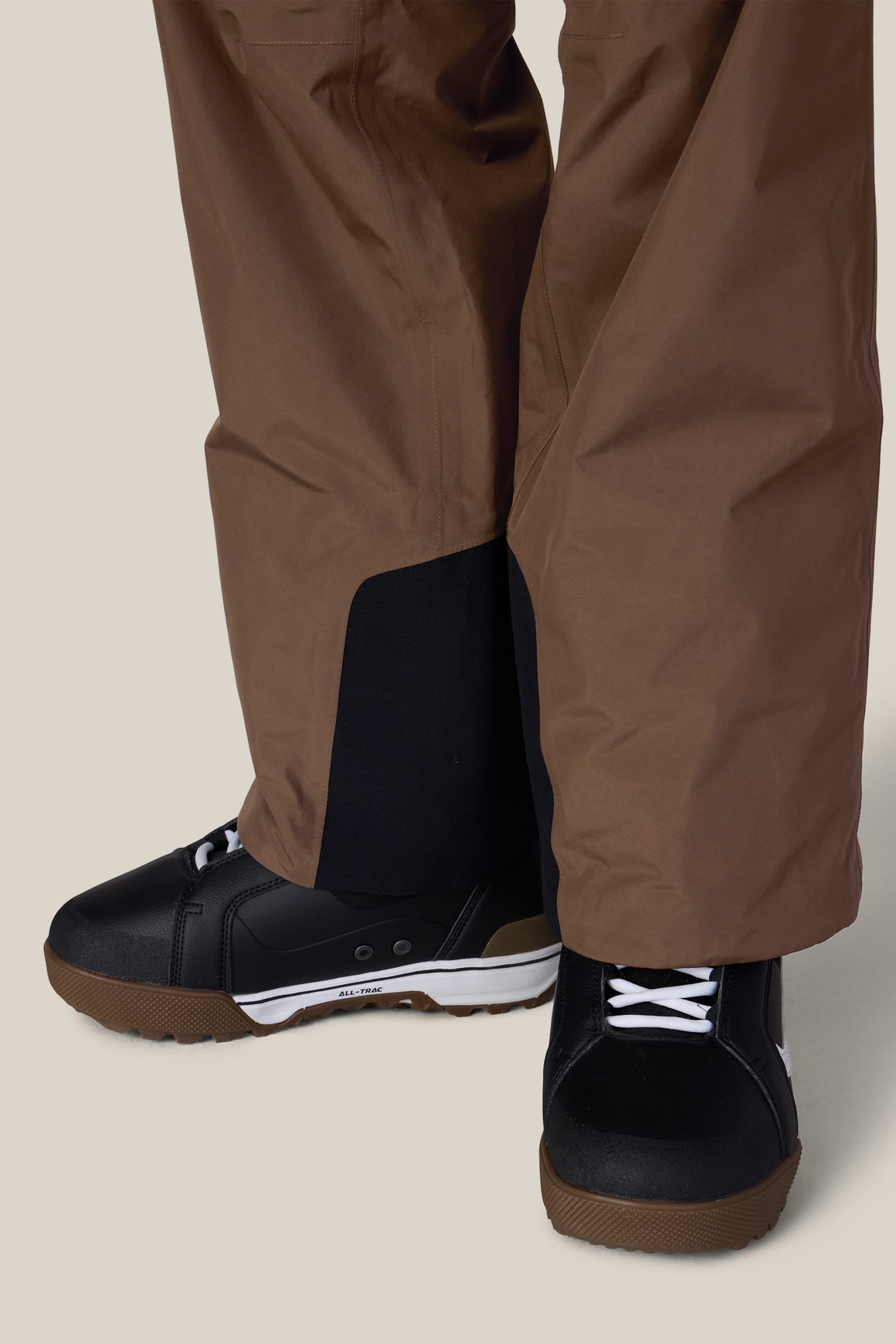 A person wearing the 686 Men’s GORE-TEX® Core Shell Pant, paired with black sneakers featuring white laces and soles, stands on a neutral background.
