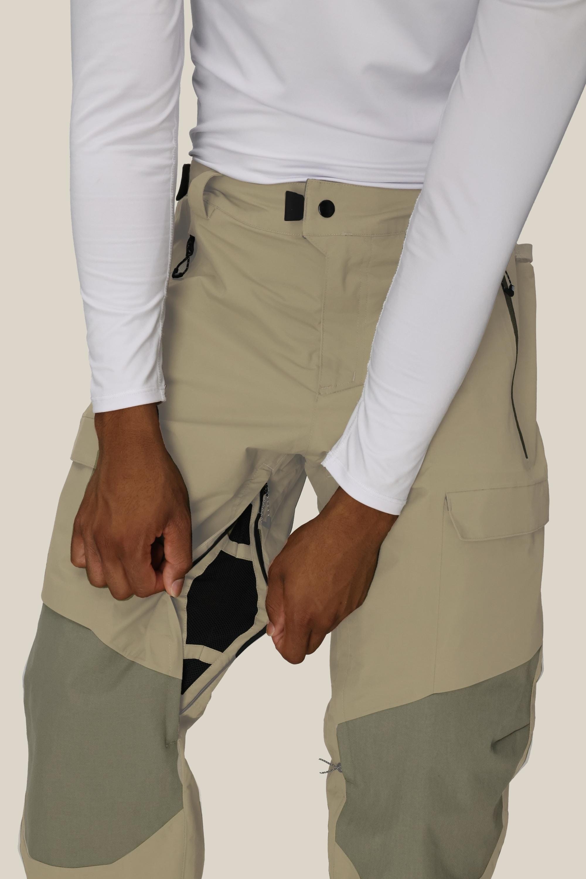 Someone wearing a 686 Men's GORE-TEX Dispatch™ Shell Pant and a white long-sleeve shirt is unzipping the vertical inner thigh zipper of the waterproof pants, revealing the mesh lining inside.