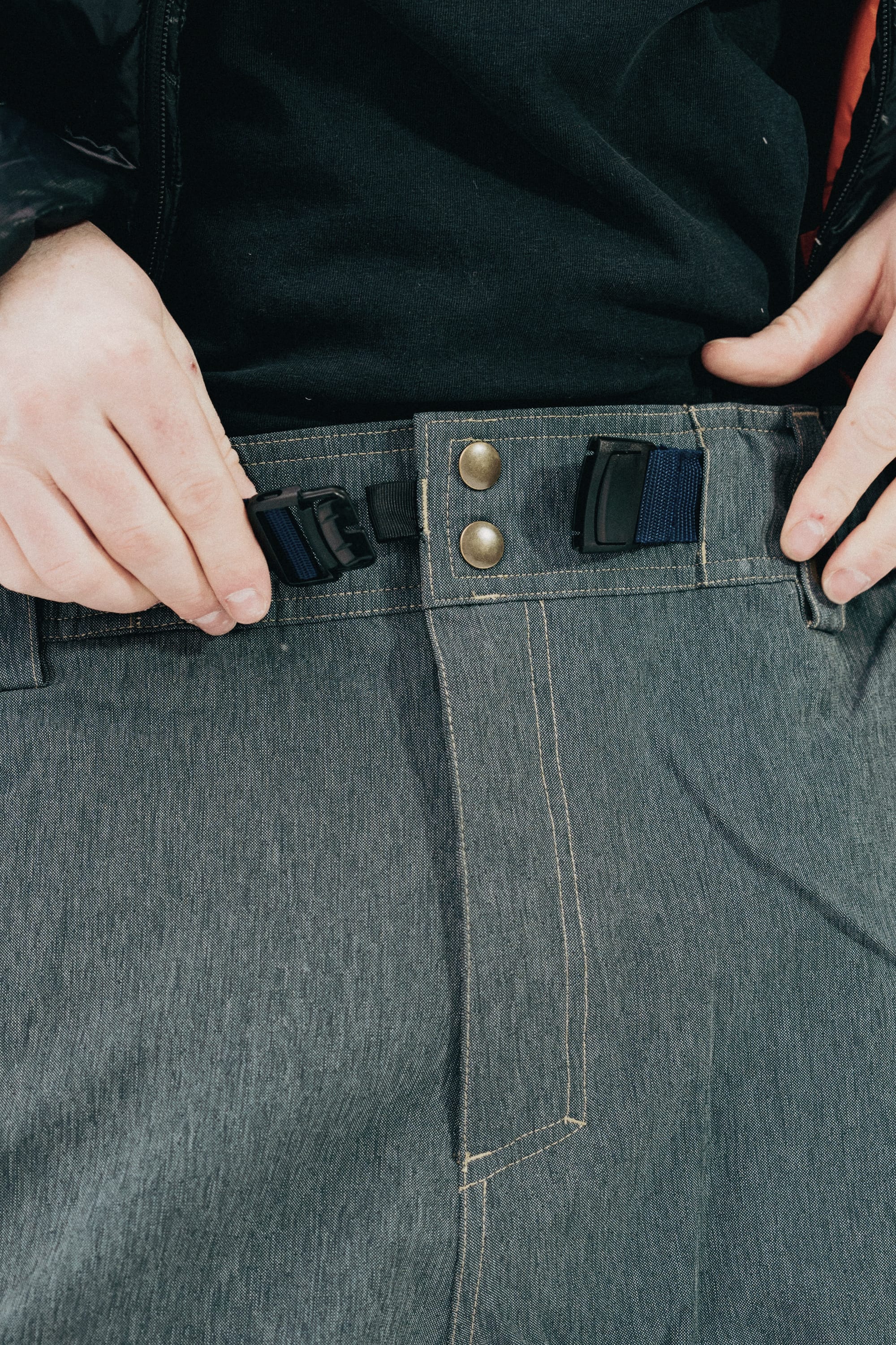 A person in gray 686 Dojo® Pants adjusts the black buckle belt at the waistband, holding each side of the unclasped buckle.