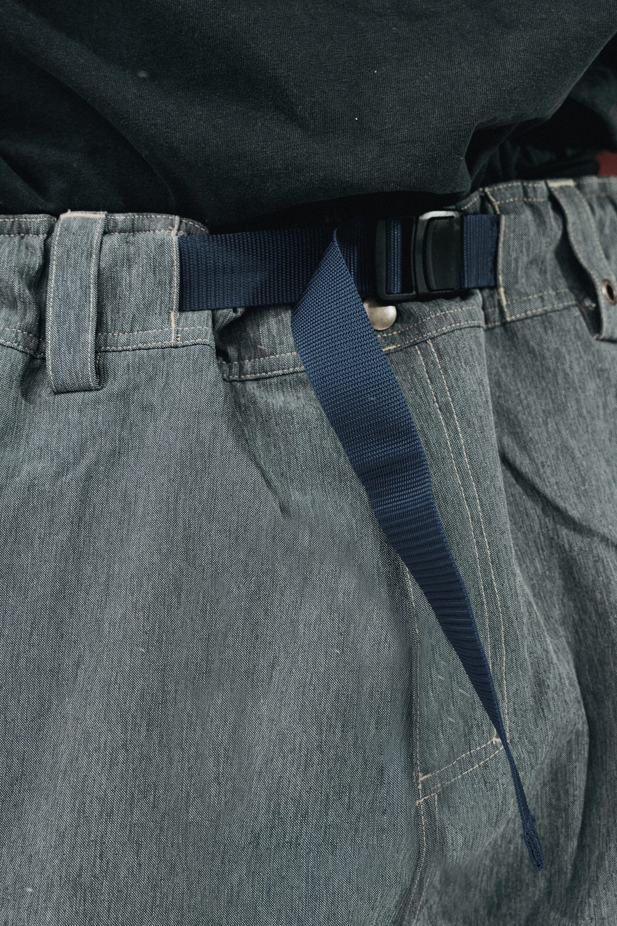 Close-up of a person wearing the 686 Dojo® Pant by 686 in light gray with a navy fabric belt and black shirt, with the belt end hanging over the front.