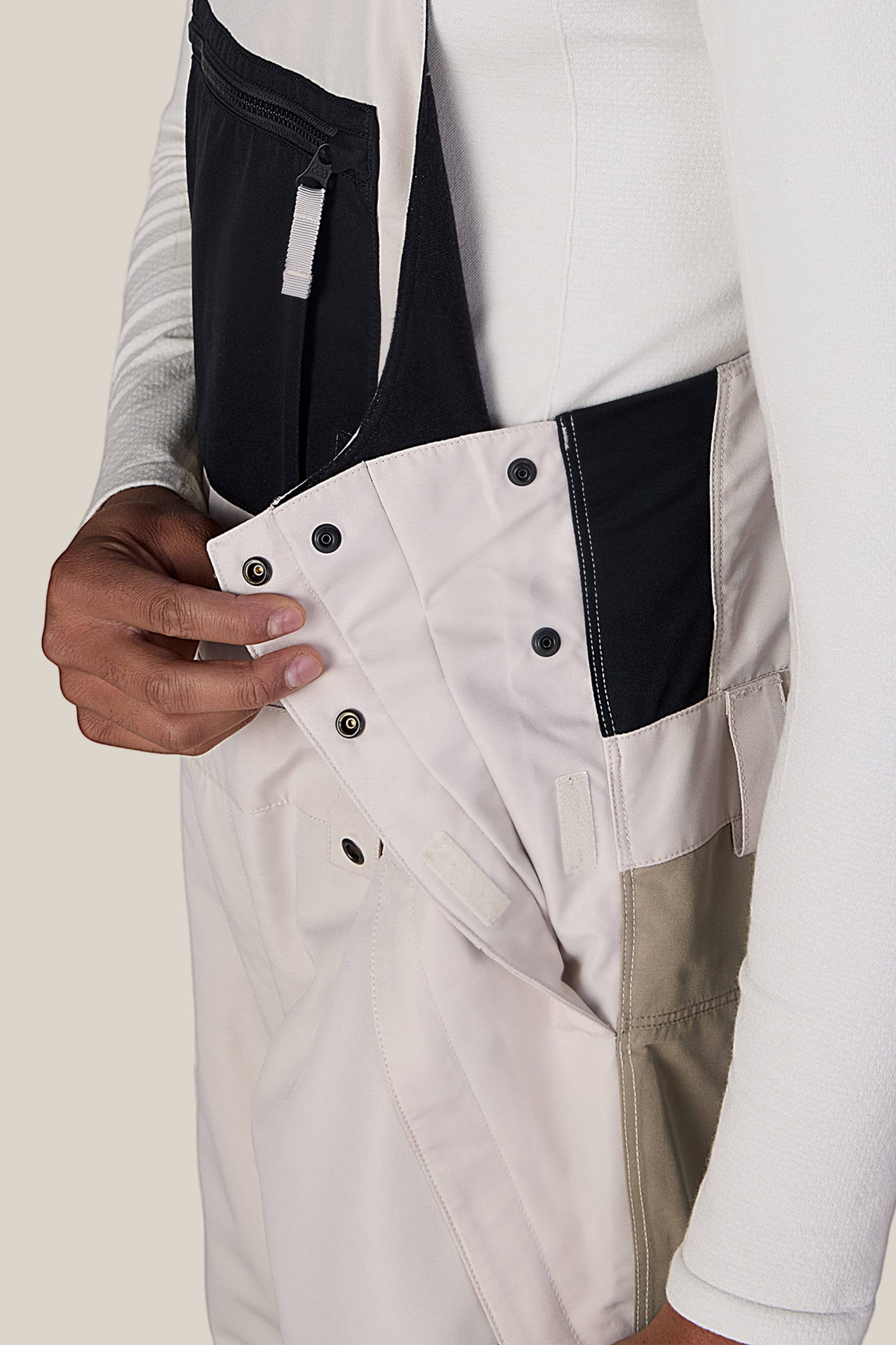A person wearing the 686 Men’s Hot Lap™ Insulated Bib opens the side buttons and Velcro closure near the waist, revealing the fastening details of these 686 overalls.