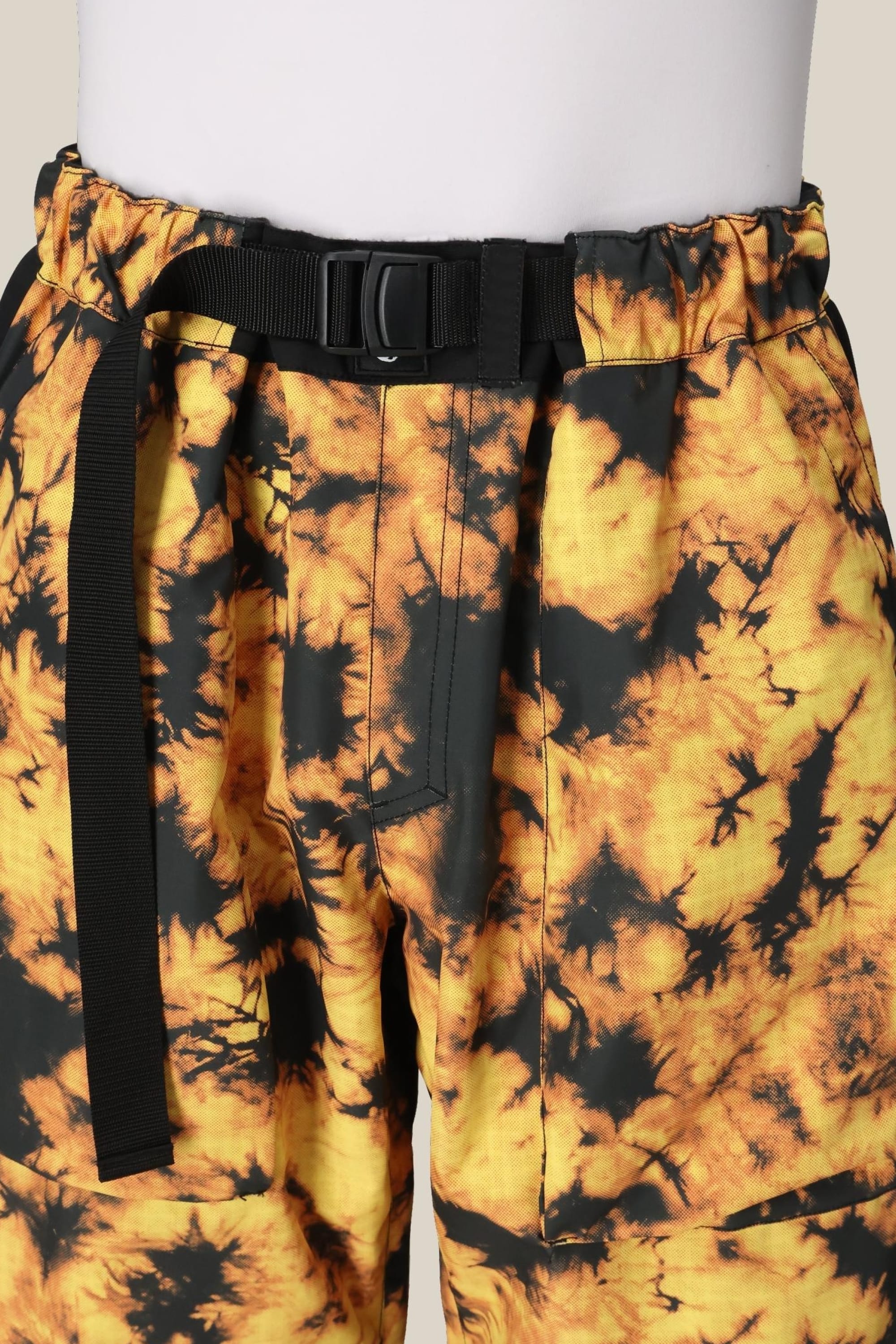 Close-up of a person wearing 686 Mens Sublime Shell Pants in yellow and black tie-dye, featuring an integrated black belt with plastic buckle, elastic waistband, and visible seam detailing for comfort and style.