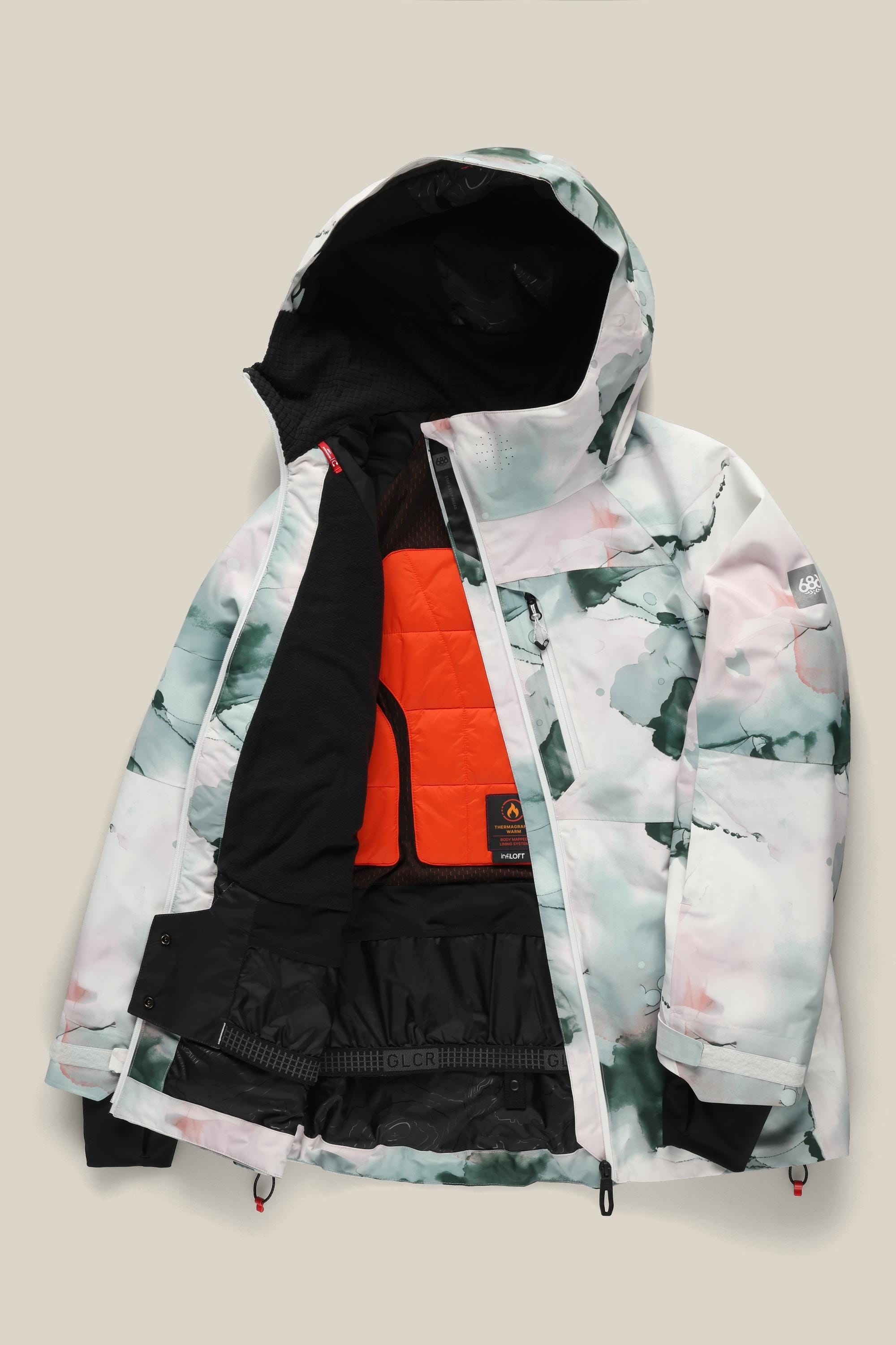 The 686 Women's Hydra™ Thermagraph® Jacket by 686 features a white, green, and pink abstract pattern, partially unzipped to show an orange lining, black snow skirt, and attached hood.