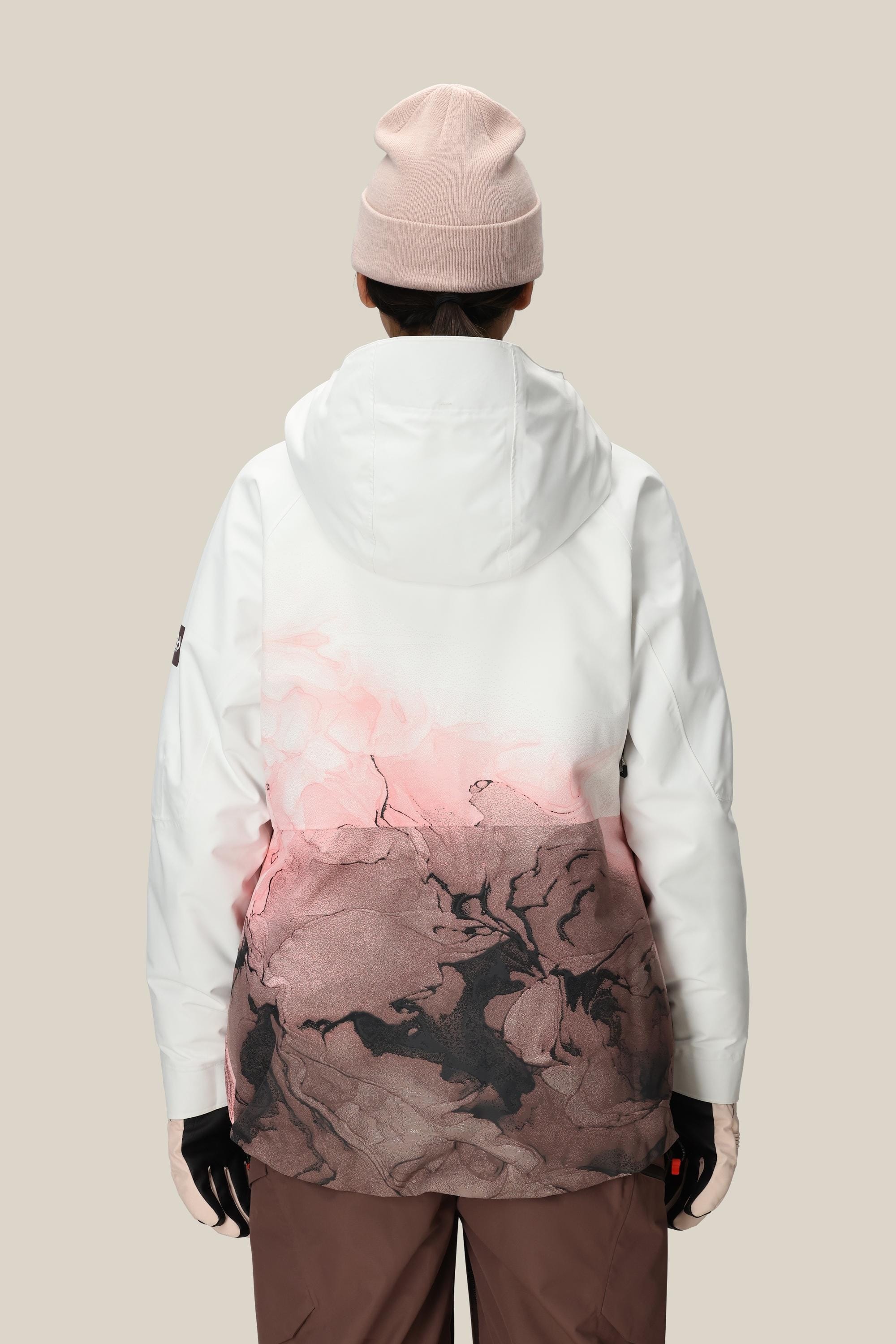 A person stands with their back to the camera, wearing a light pink beanie, brown pants, black gloves, and the 686 Women's Hydra™ Thermagraph® Jacket by 686 in white and pink patterns, set against a plain beige background.