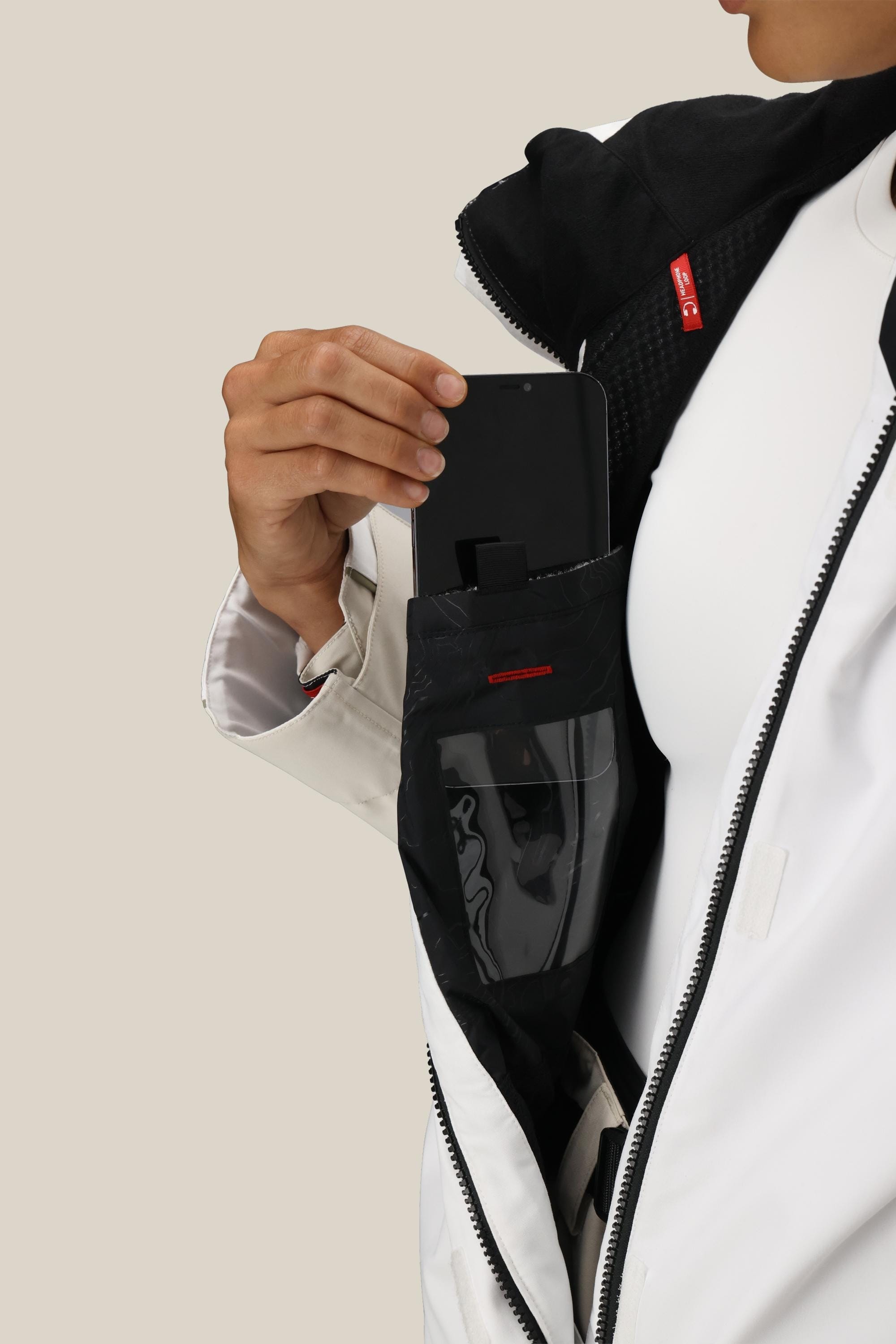 A person puts a black smartphone into the transparent inner pocket of the 686 Women's Hologram™ Shell Jacket, partially unzipped to reveal the sleek lining.