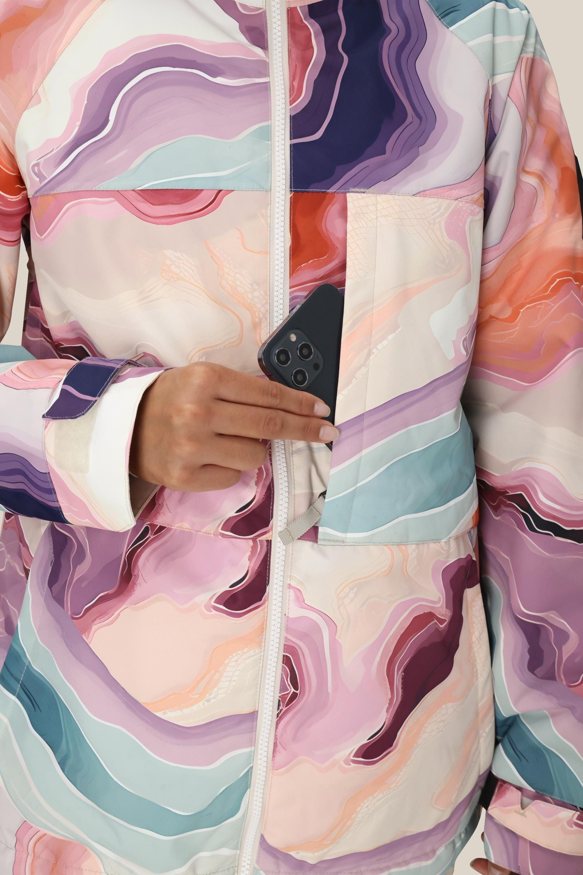 A person wearing the 686 Women's Athena™ Insulated Jacket with a wavy pattern places a black smartphone into the chest pocket. Only their torso and hand are visible.