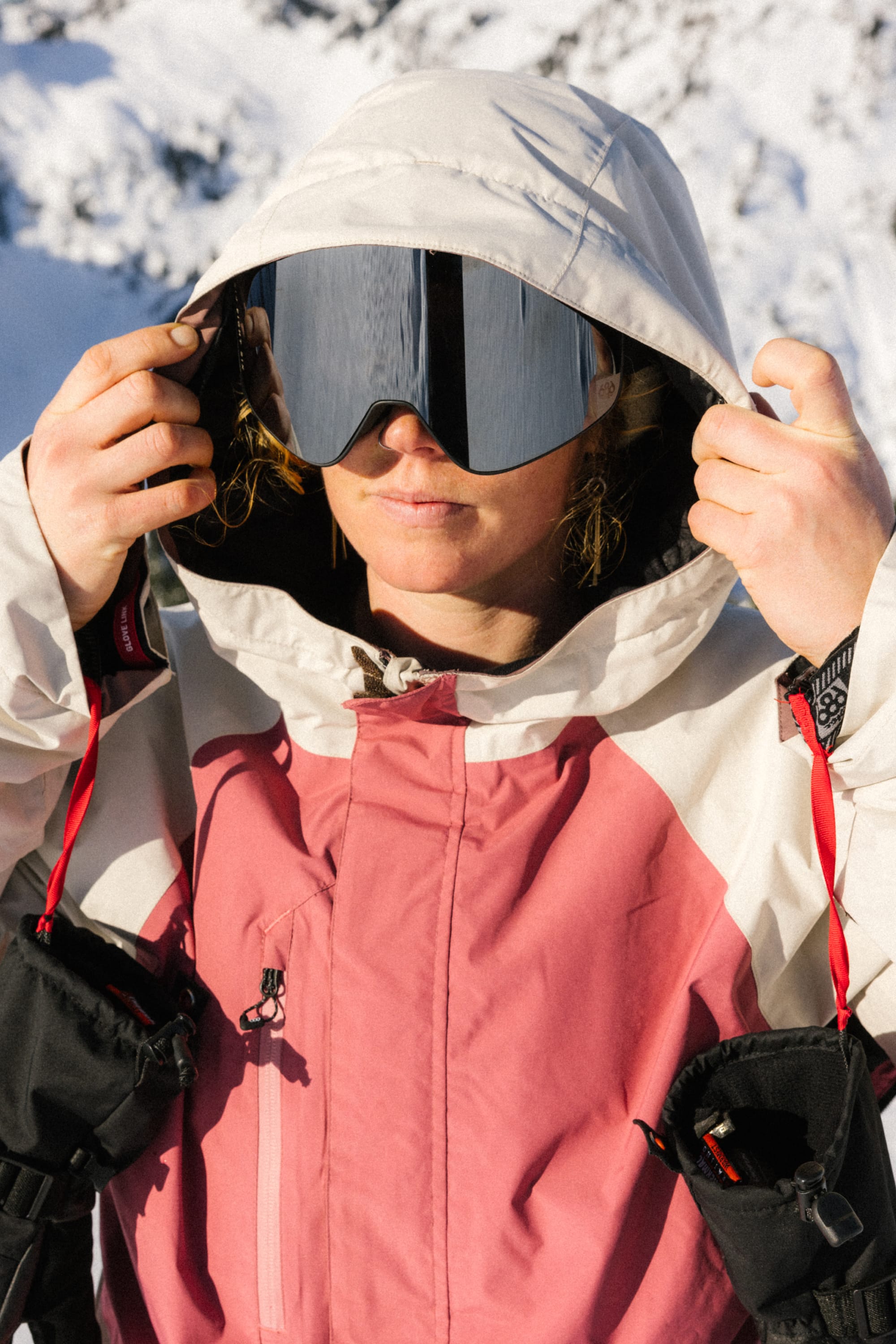 Wearing the 686 Women's GORE-TEX Willow™ Insulated Jacket, a person adjusts their hood and ski goggles against a backdrop of snowy mountains.