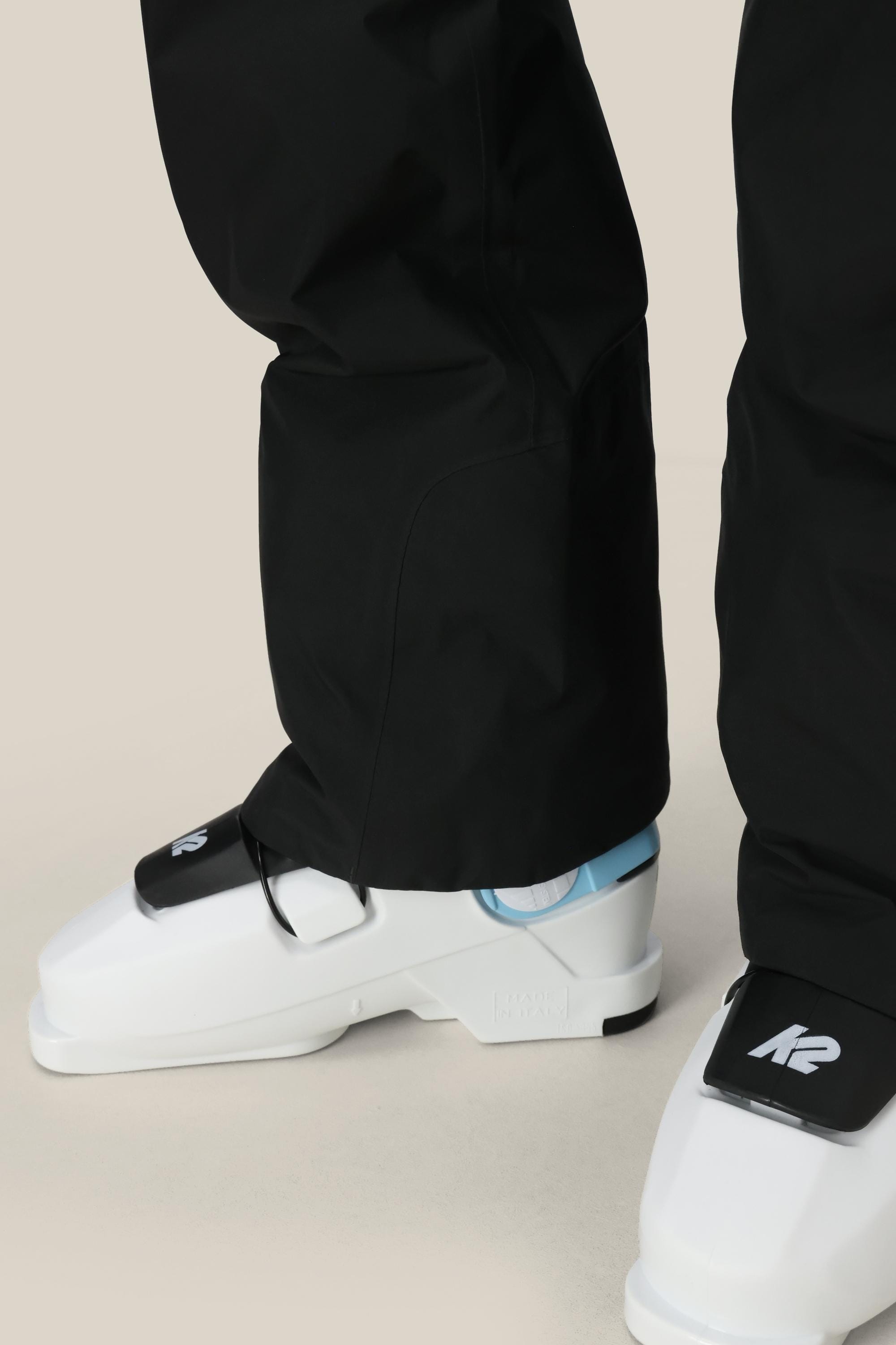 A person wearing 686 Women's GORE-TEX Willow™ Insulated Pant stands on a light-colored surface, paired with white ski boots featuring black straps and the K2 logo.