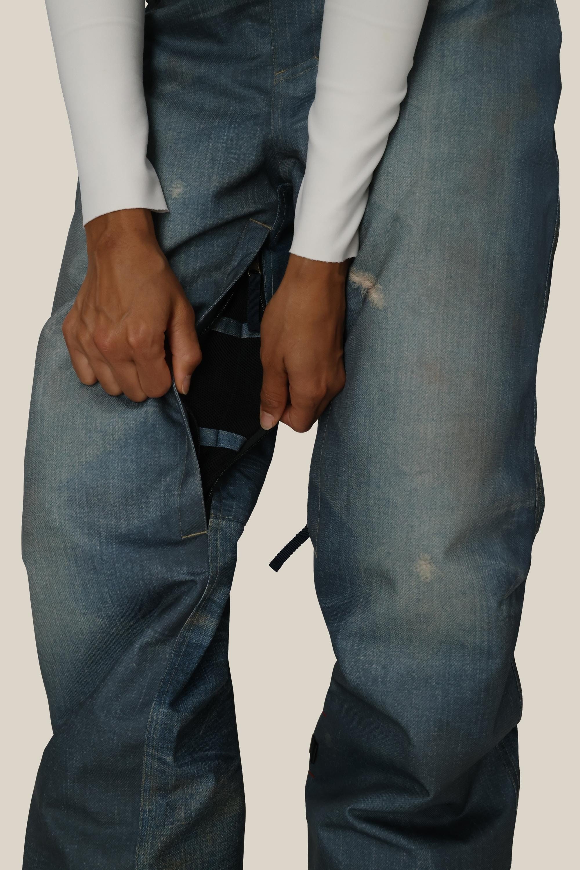 A person wearing a white long-sleeve shirt and blue jeans unzips the front of their pants, revealing 686 Women's Deconstructedª Denim Insulated Pants by 686, made from durable waterproof polyester fabric underneath.