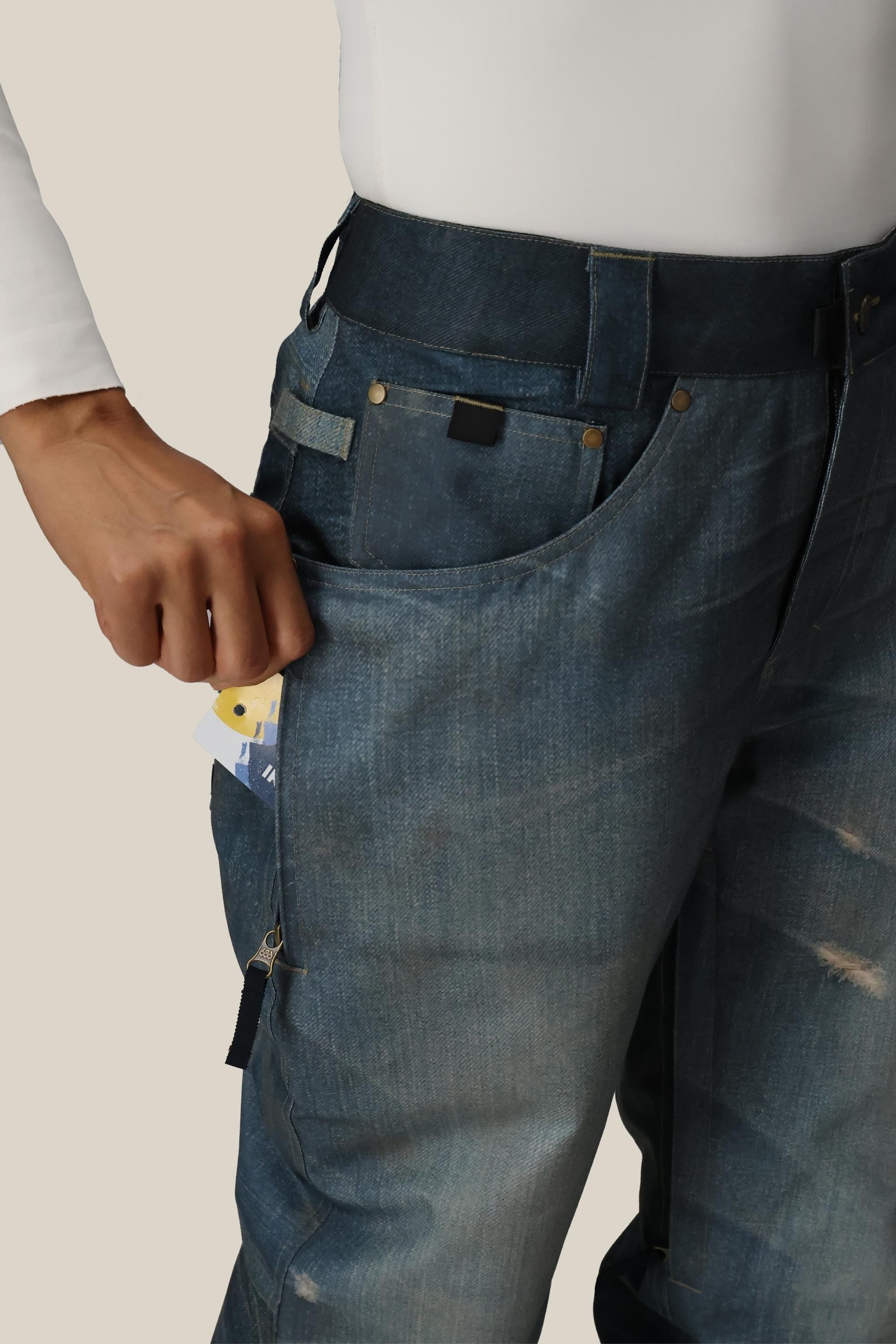 A person wearing the 686 Women's Deconstructed™ Denim Insulated Pant places a credit card into the zippered front pocket of these waterproof pants.