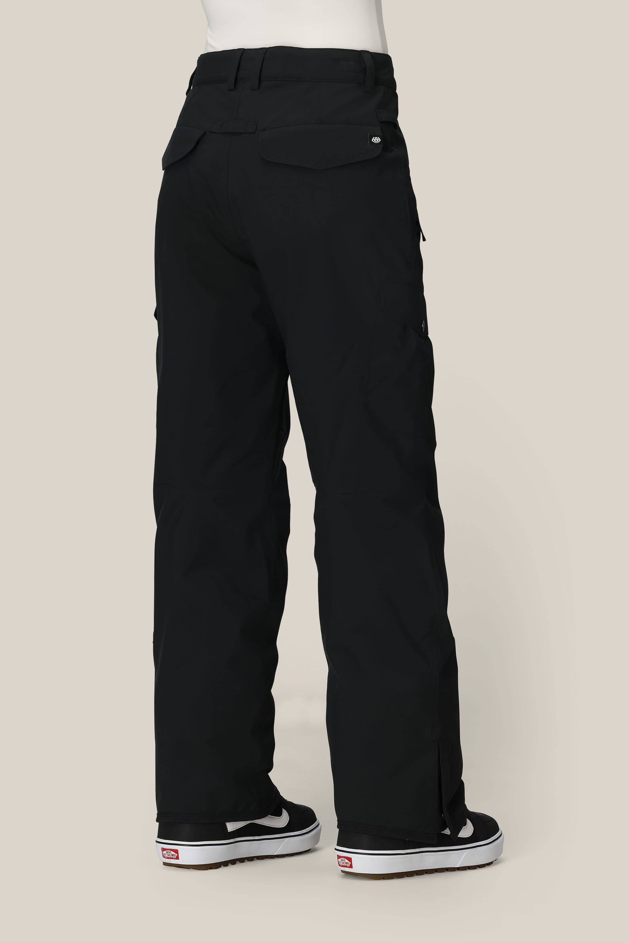 A person is seen from behind wearing 686 Women's Aura™ Insulated Cargo Pant by 686 and black-and-white skate shoes, standing against a plain beige background.