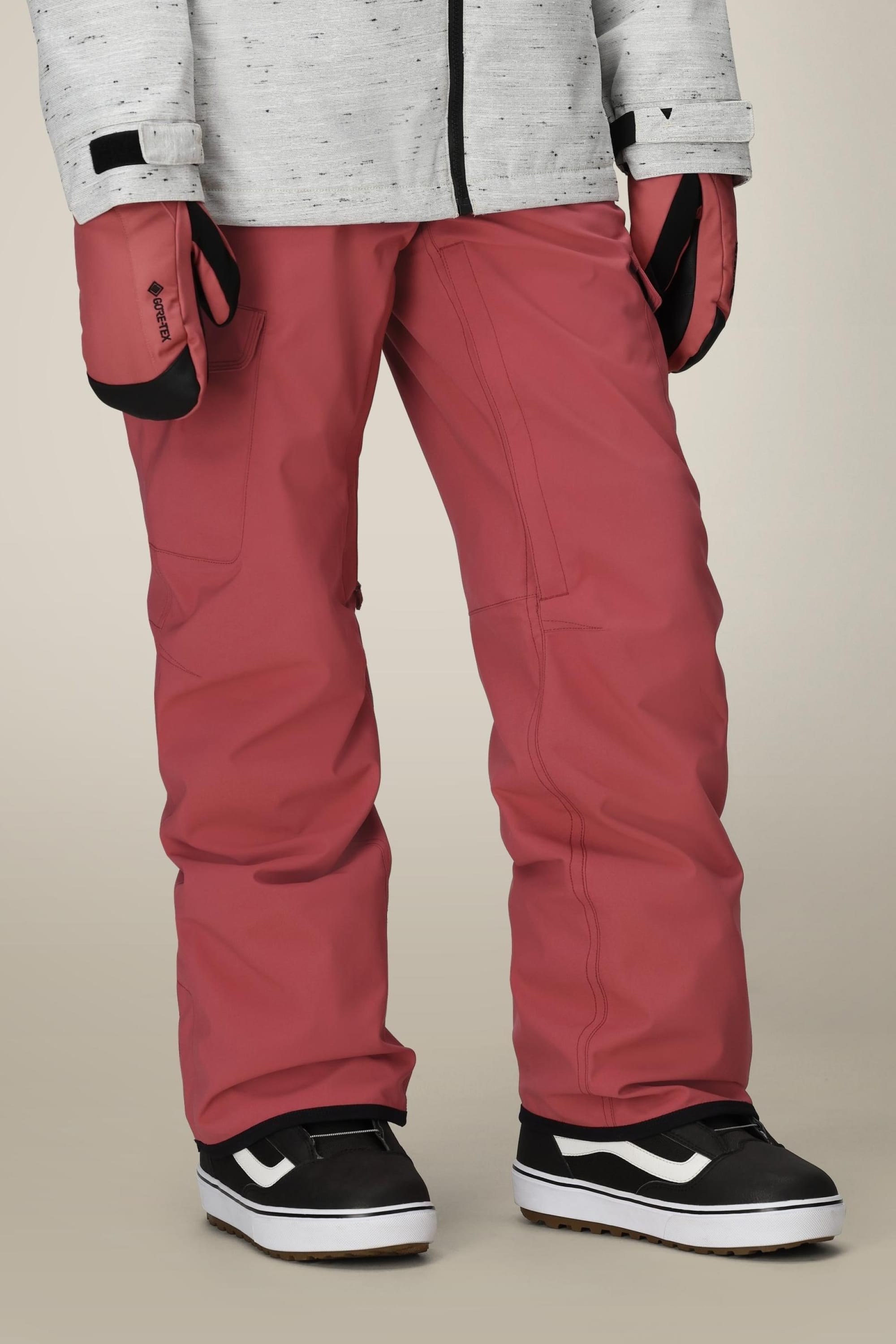 A person wearing the 686 Women's Aura™ Insulated Cargo Pant in dusty rose, paired with a light gray jacket, matching mittens, and black-and-white sneakers, shown from shoulders down against a neutral background.