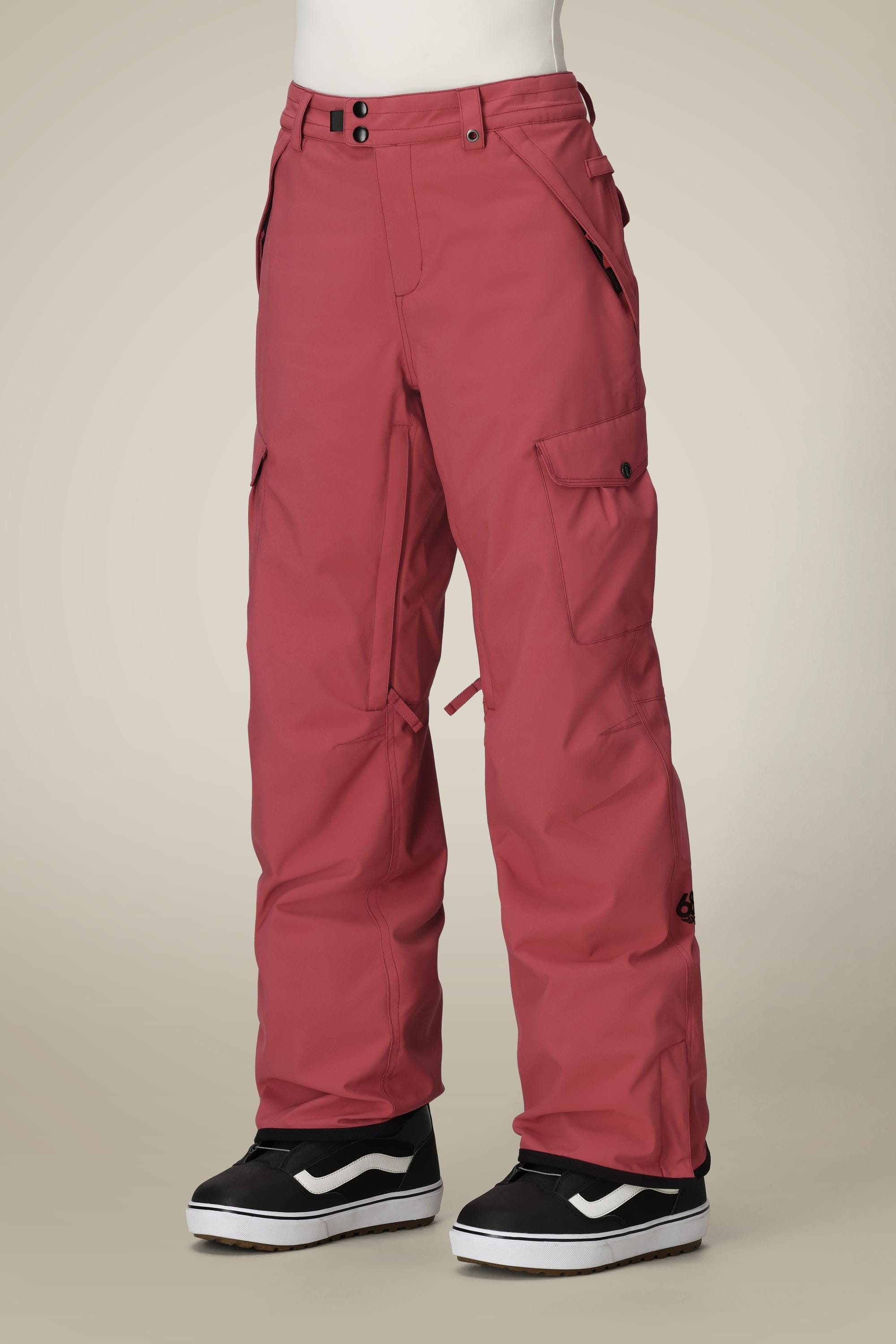 A person wearing 686 Women's Aura™ Insulated Cargo Pant in rose red and black-and-white Vans sneakers stands against a plain beige background, with only their lower body visible.