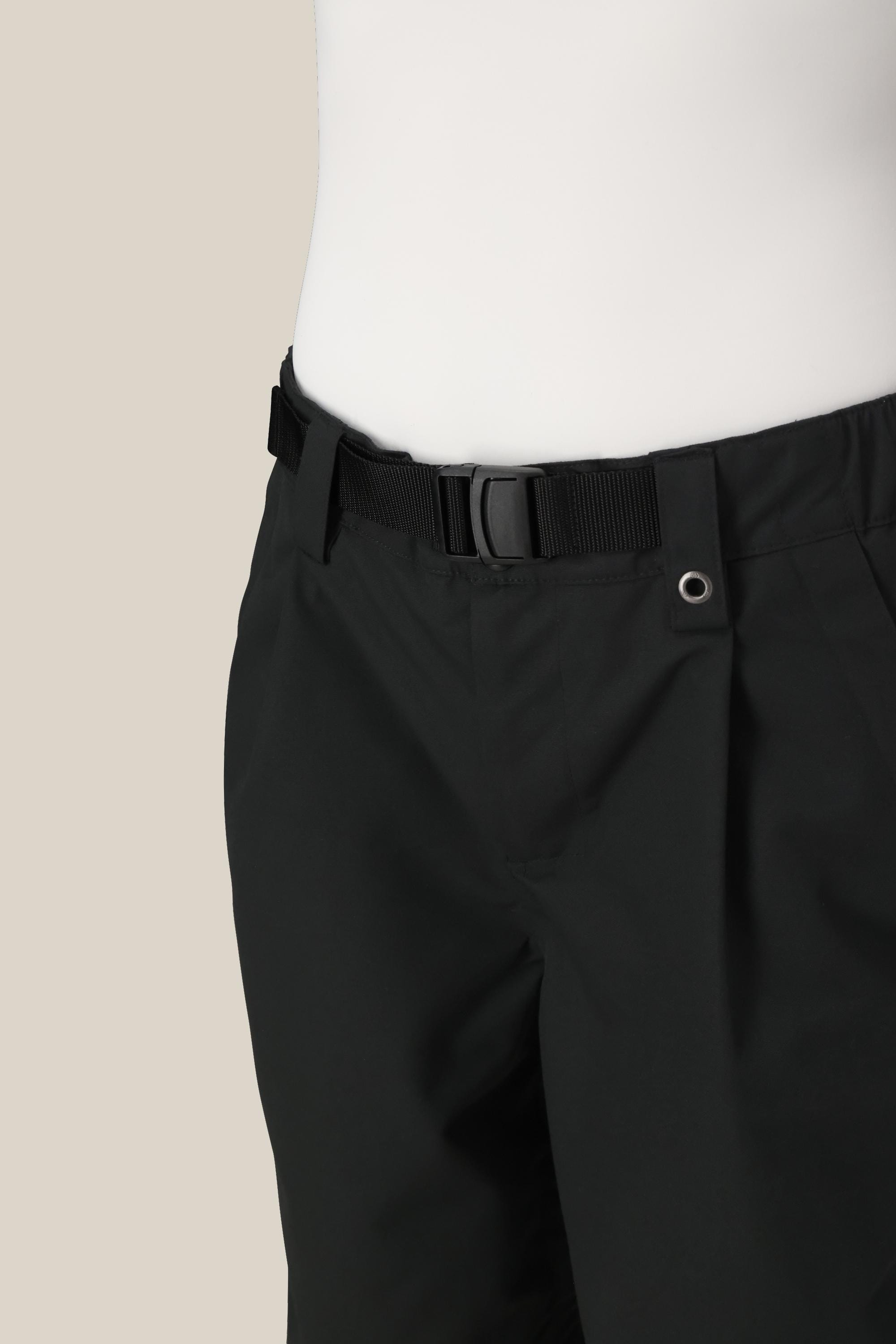 A close-up of a person wearing 686 Women's Outline™ Shell Pant. The photo focuses on the waist and upper thighs, highlighting the black buckle, metal grommet near the waistband, and features a plain beige background.