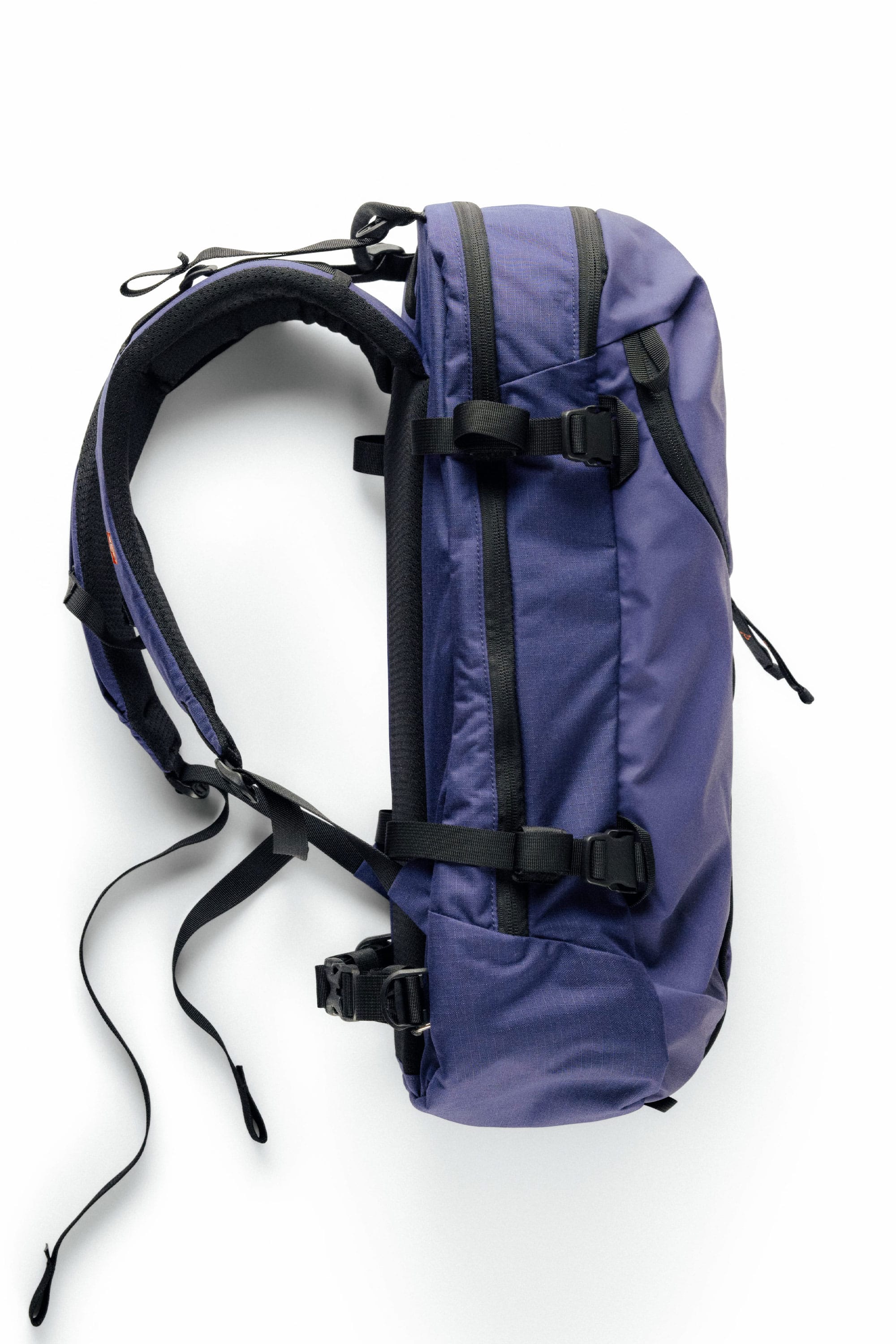 The 686 Mystery Ranch x 686 Qi 22L Snow Pack is shown in purple with black straps and buckles, photographed from the side on a white background. It features padded shoulder straps and multiple adjustment points.