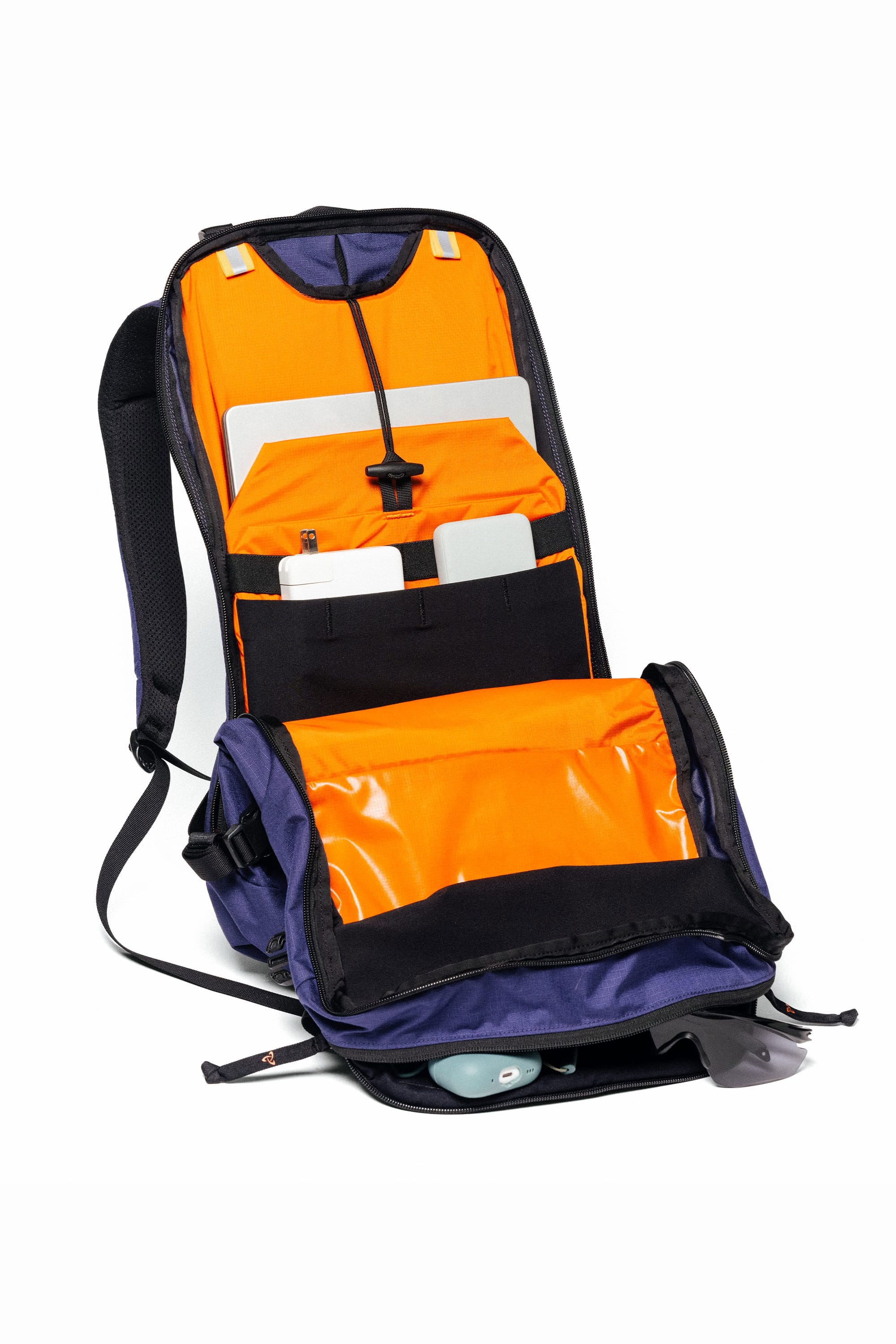 The 686 Mystery Ranch x 686 Qi 22L Snow Pack by 686 features an open main compartment with an orange interior, multiple pockets holding a laptop, tablet, and accessories such as sunglasses and a computer mouse.