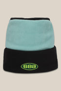 The 686 Flatop Fleece Hat is an acrylic knit beanie with a light blue top, black folded brim, and a green/yellow 686 logo on the front. Set against a plain beige background.