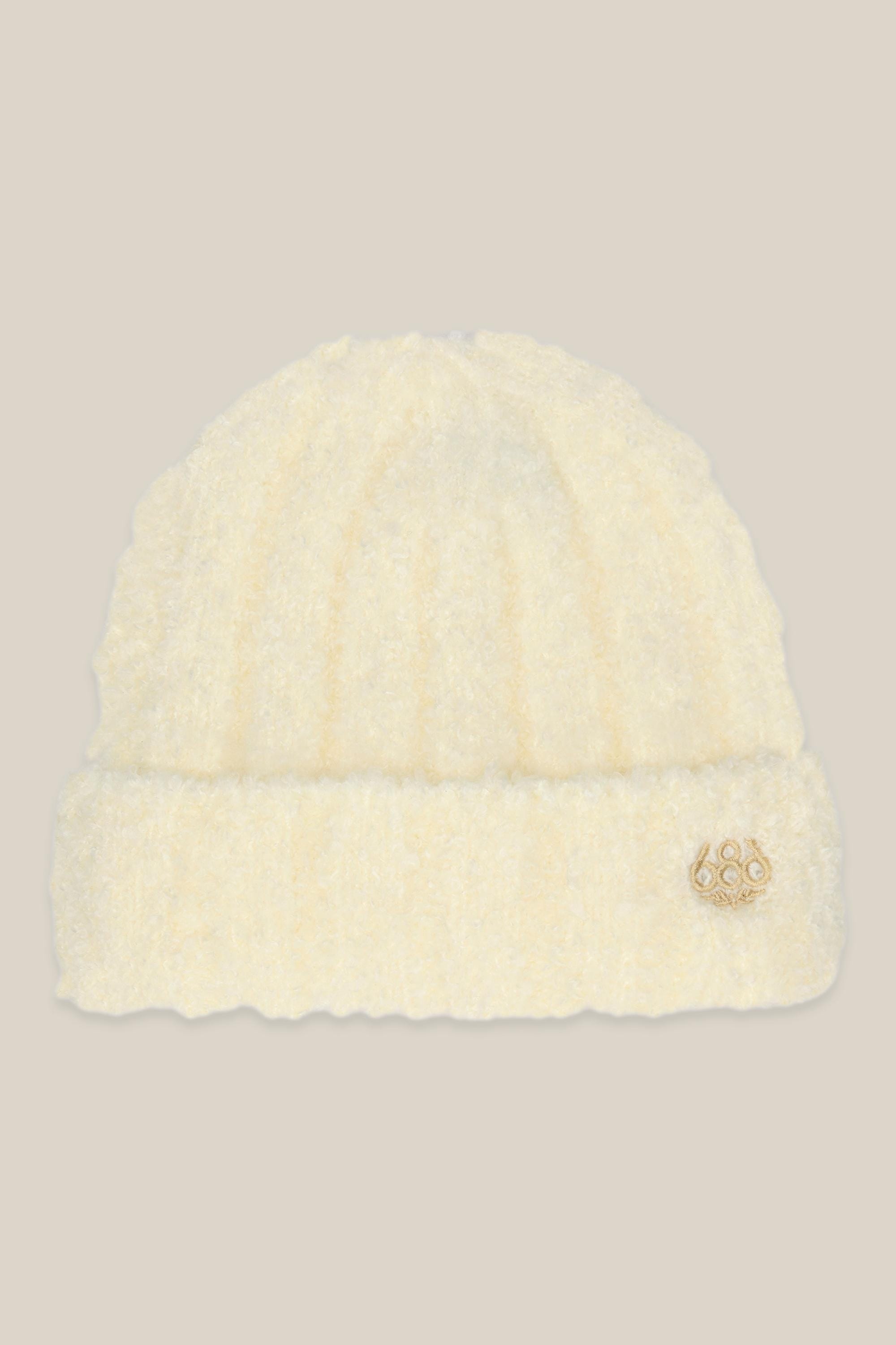 The 686 Womens Fuzzy Beanie by 686 is a soft, off-white beanie for women featuring a folded brim and a small gold circular emblem on the front, shown against a beige background.