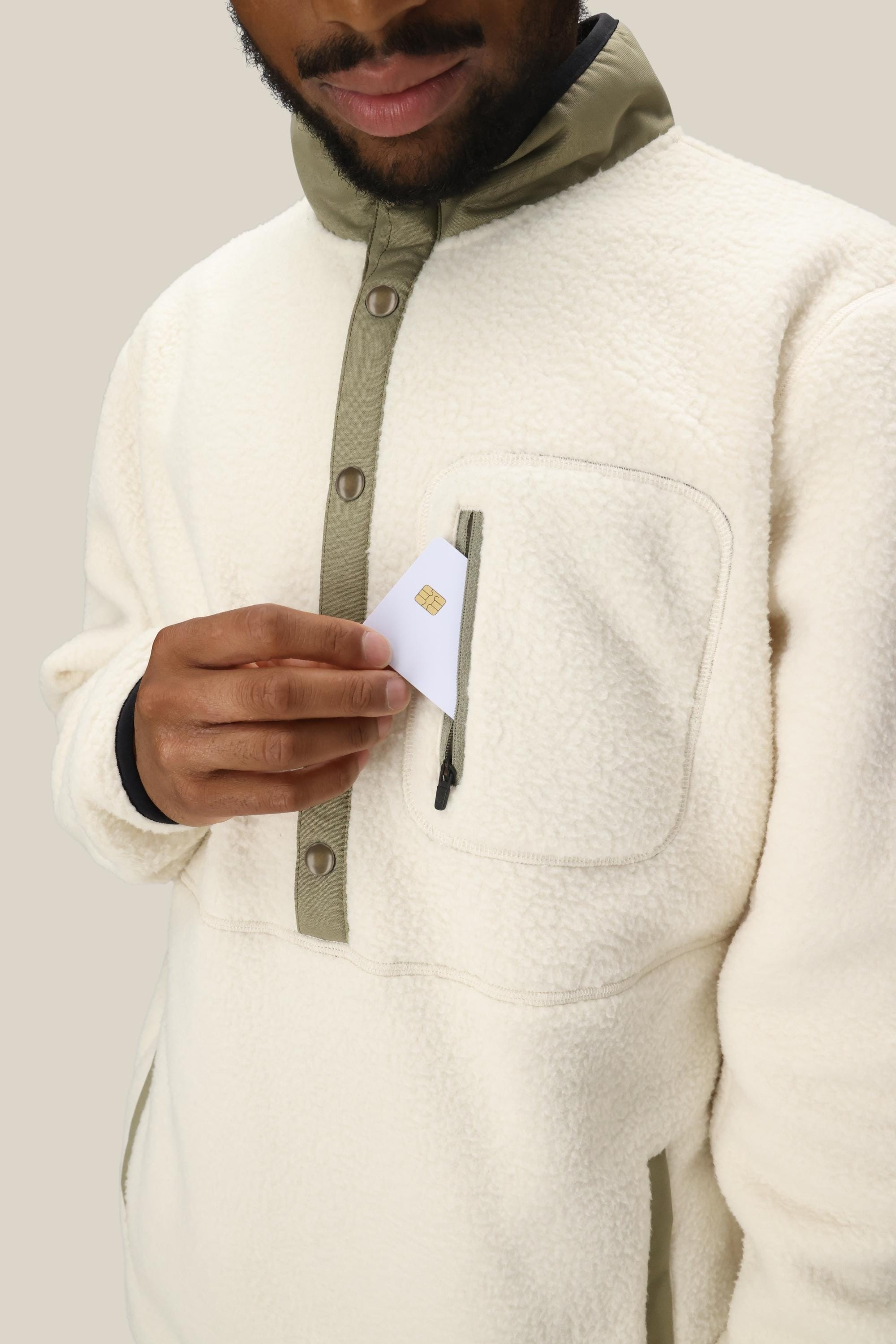 A person wearing the 686 Mens Tioga Fleece Pullover places a white card with a gold chip into the garments zipped chest pocket.