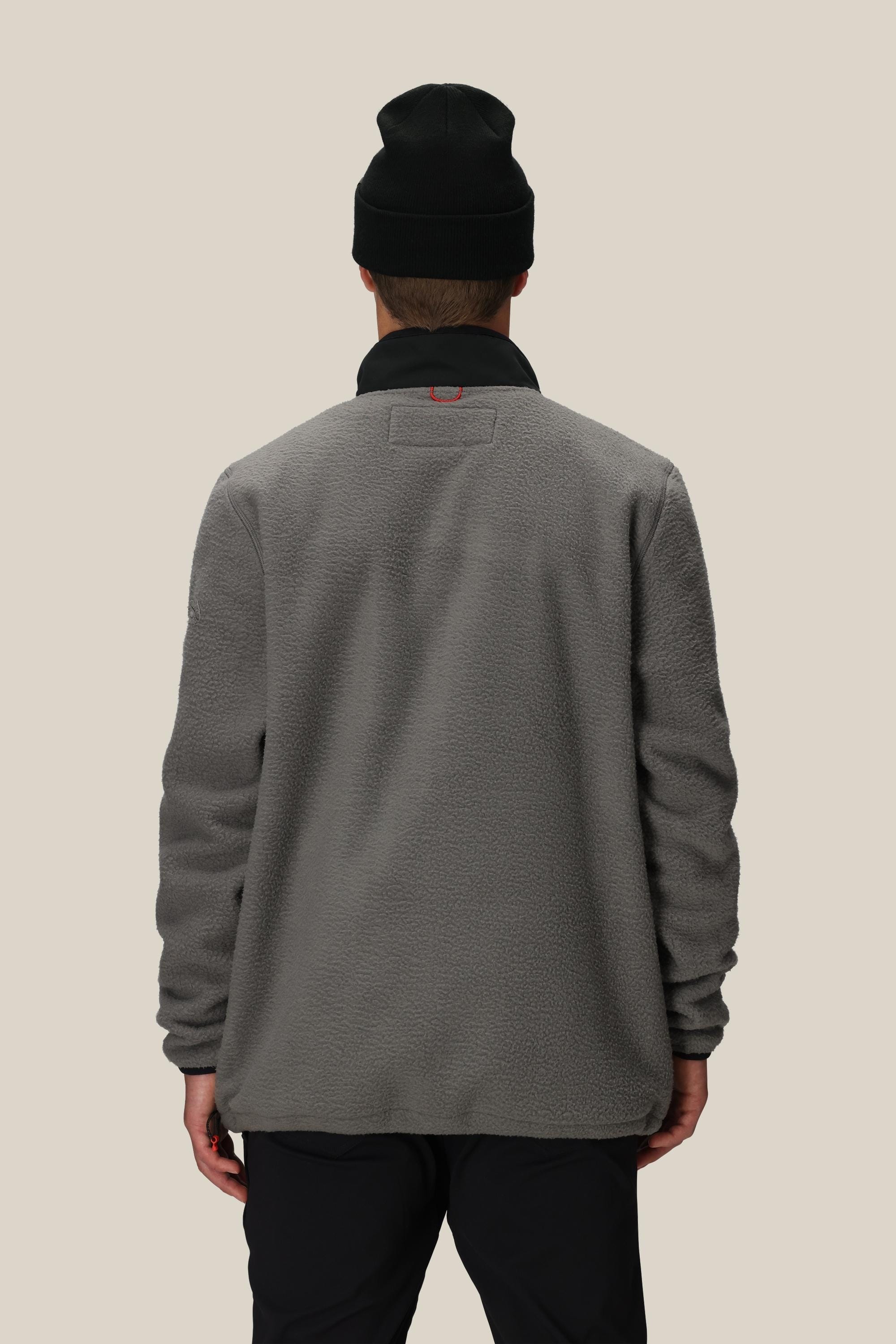 A person wearing a black beanie and the 686 Mens Tioga Fleece Pullover by 686 stands with their back to the camera against a plain beige background.