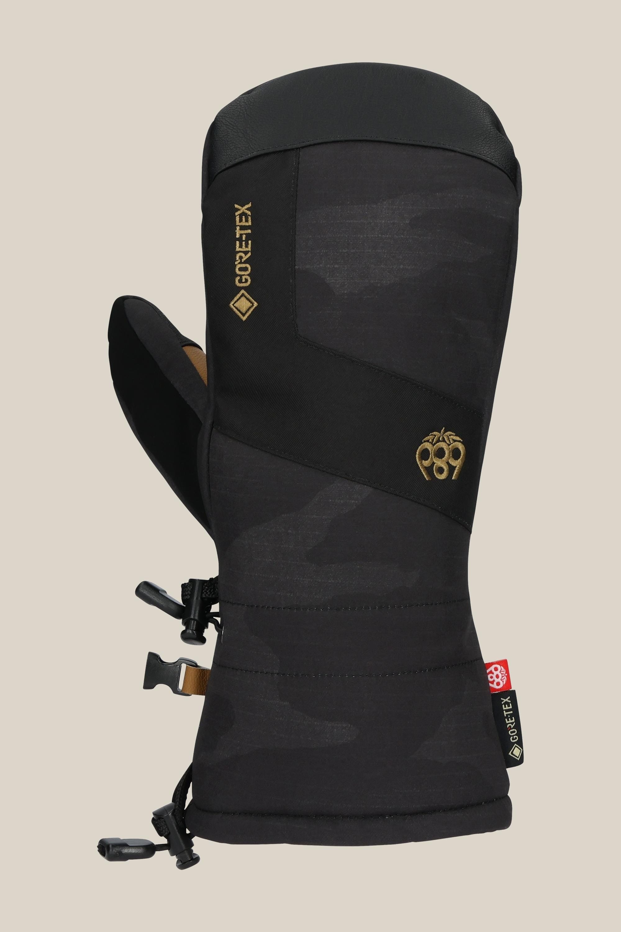 The 686 Men's GORE-TEX Linear™ Mitt by 686 features a black camo design, durable poly/PU build, Gore-Tex branding, adjustable wrist strap, drawstring closure, and a small cuff logo—ideal for cold weather adventures.