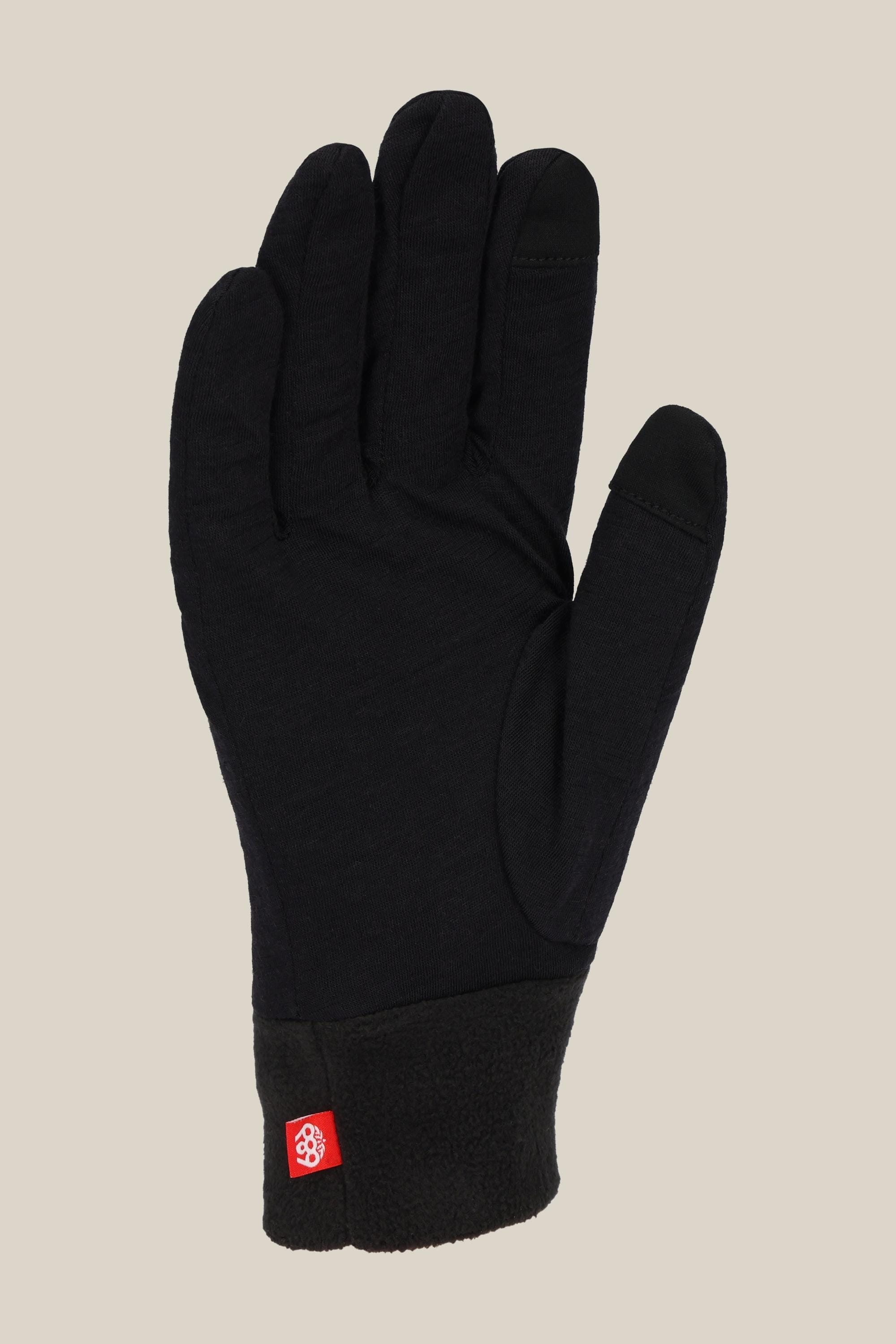 The 686 Mens Merino Glove Liner by 686 is shown in black with a textured cuff and a small red tag near the wrist, palm up on a plain beige background.