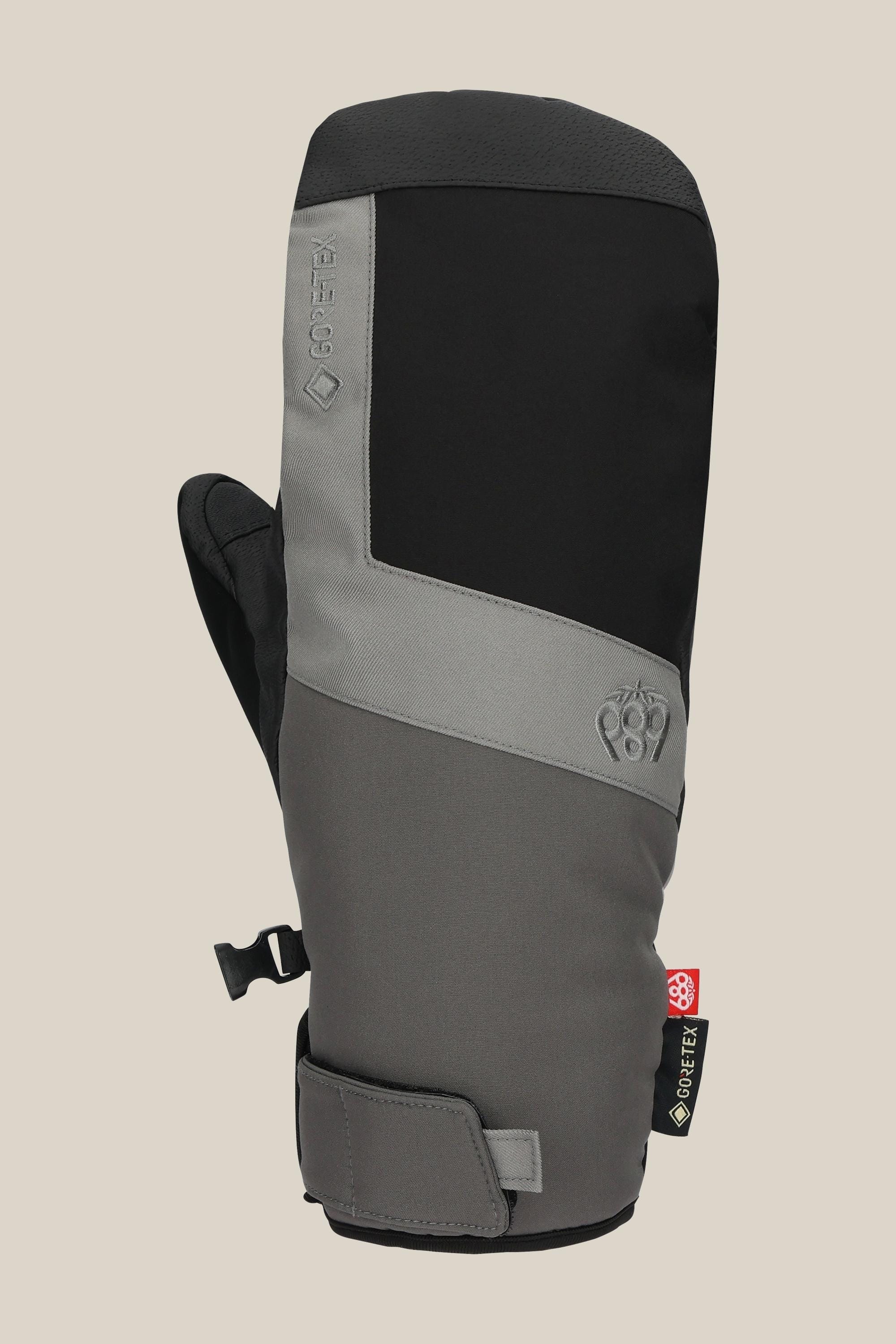 The 686 Men's GORE-TEX Linear™ Under Cuff Mitt features a black and gray color block design, black thumb, adjustable wrist strap, GORE-TEX branding on the side, and is shown against a plain light beige background.