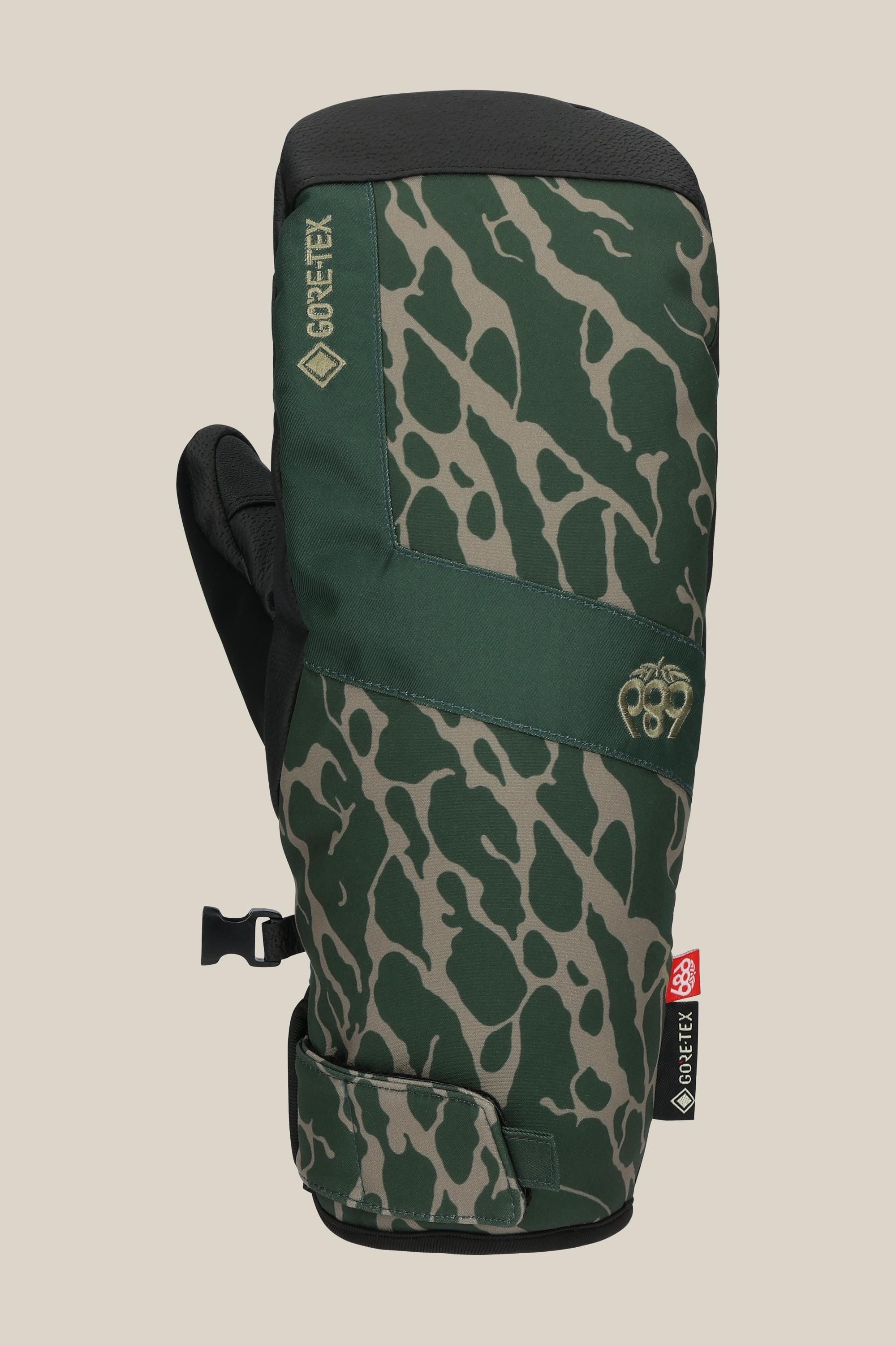 The 686 Men's GORE-TEX Linear™ Under Cuff Mitt is a durable green poly mitt with black and light green camo, black adjustable strap, GORE-TEX logo, and a red and white patch—ideal for outdoor adventures.