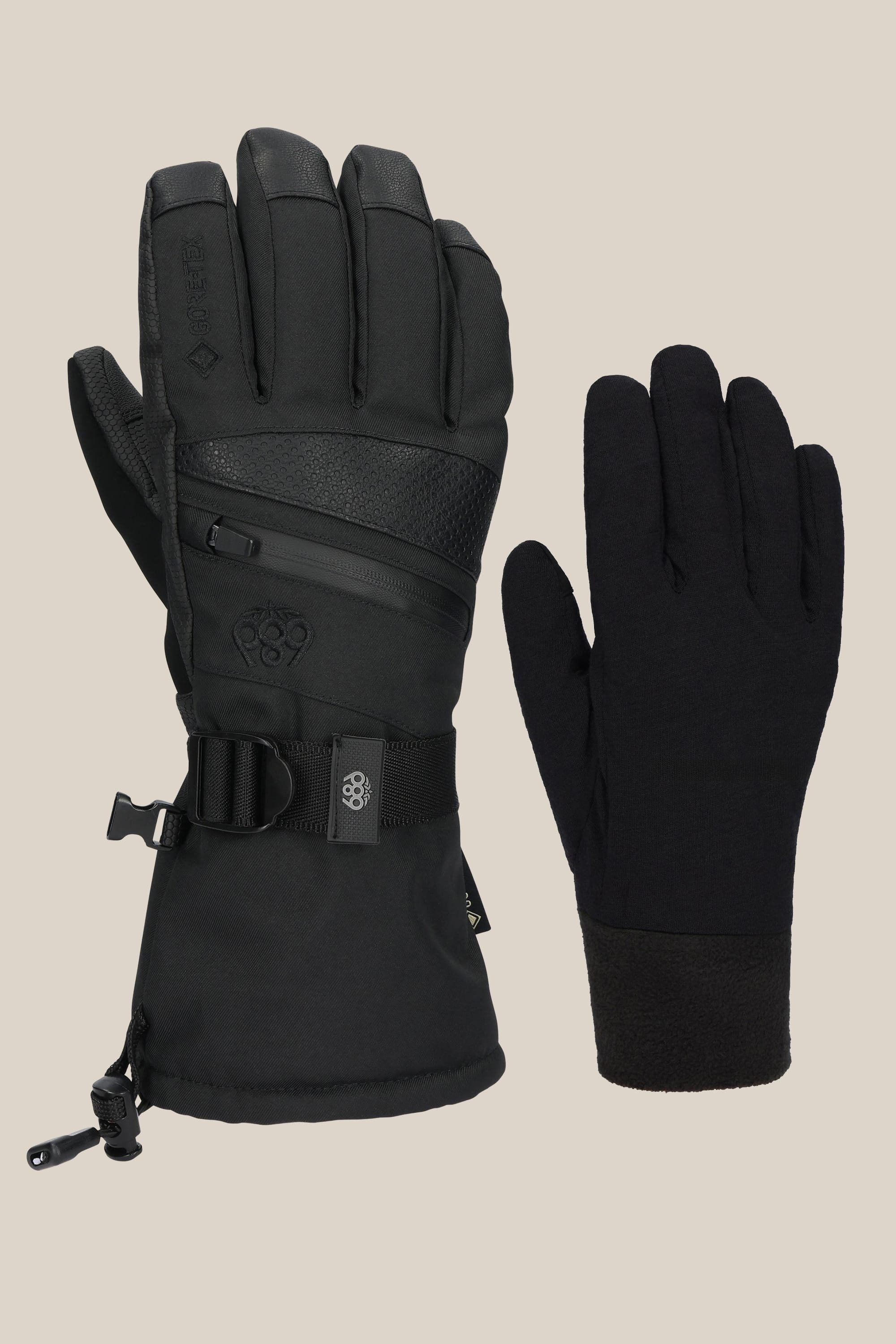 The 686 Women's GORE-TEX SMARTY® 3-In-1 Gauntlet Glove by 686 is shown in two styles—a bulkier version with wrist strap, zipper, and drawstring, and a slimmer plain PU glove—displayed on a beige background.
