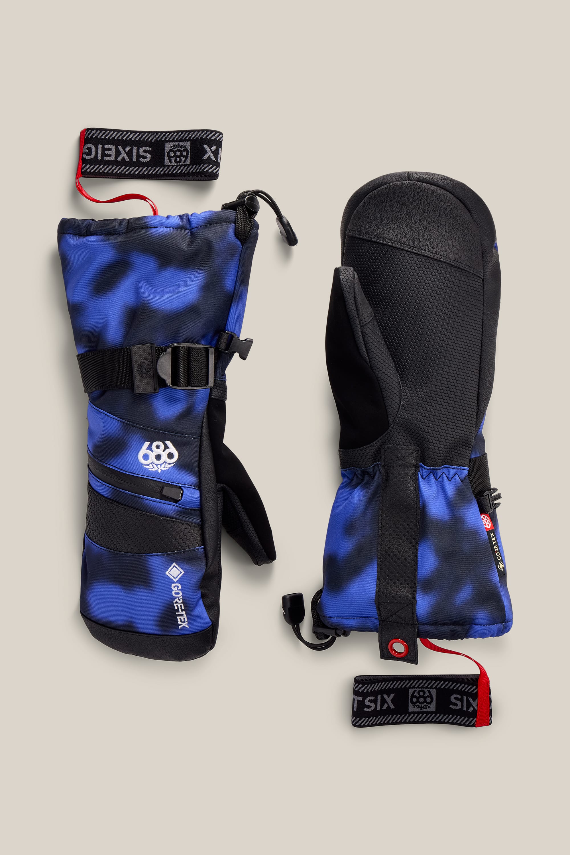 A pair of 686 Women’s GORE-TEX® SMARTY® 3-In-1 Gauntlet Mitts in blue and black, featuring wrist straps and adjustable buckles, are displayed flat on a beige background. The 686 brand logo and the word “GORE-TEX” are visible on one mitten.