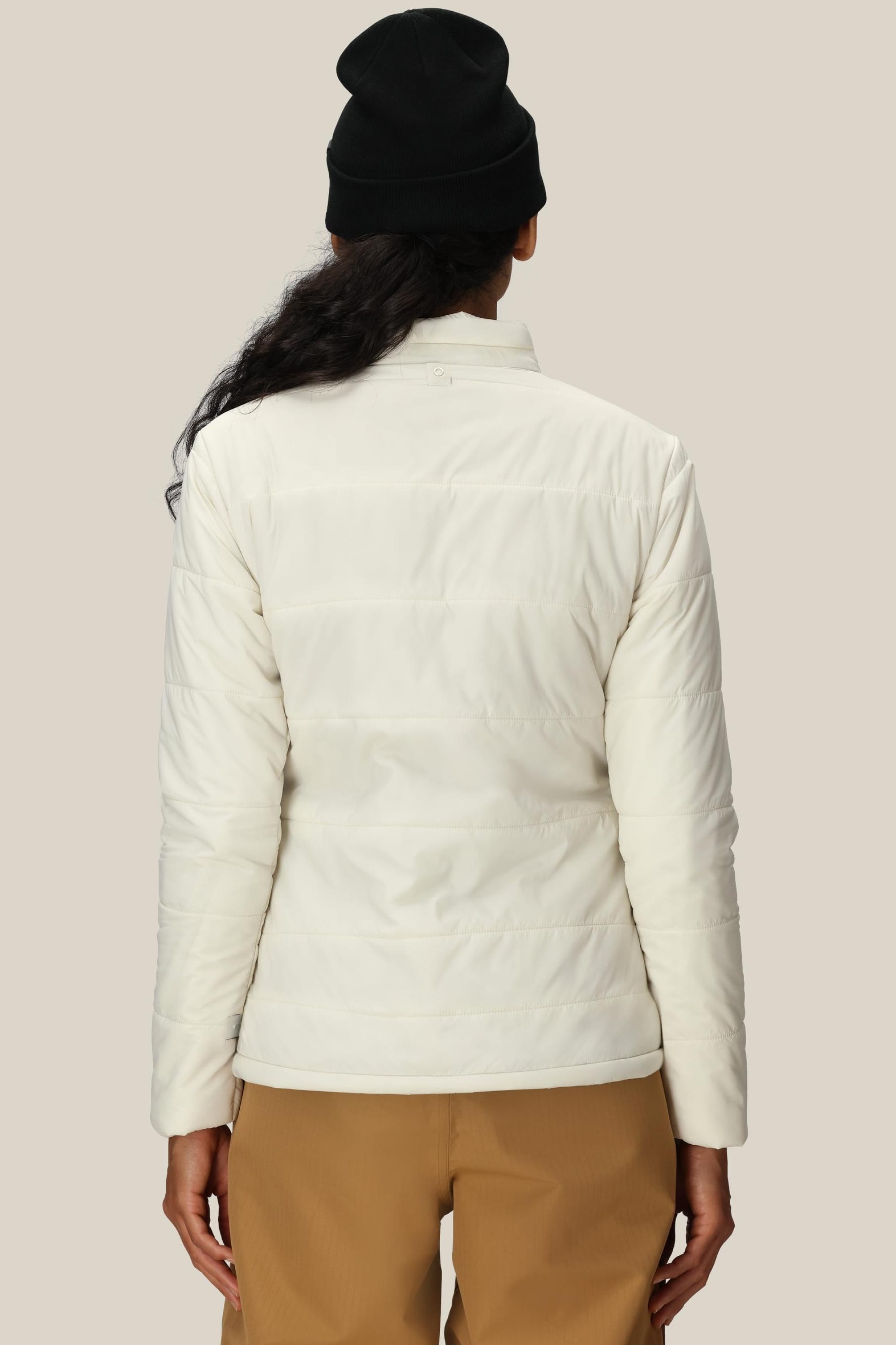 A person is shown from the back against a plain beige background, wearing tan pants, a black beanie, and the 686 Womens Thermal Puff Insulated Jacket by 686.