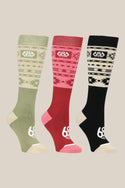 The 686 Womens Southwest Socks 3 Pack features green, red, and black acrylic socks with cream geometric patterns and logos, displayed side by side on a beige background.