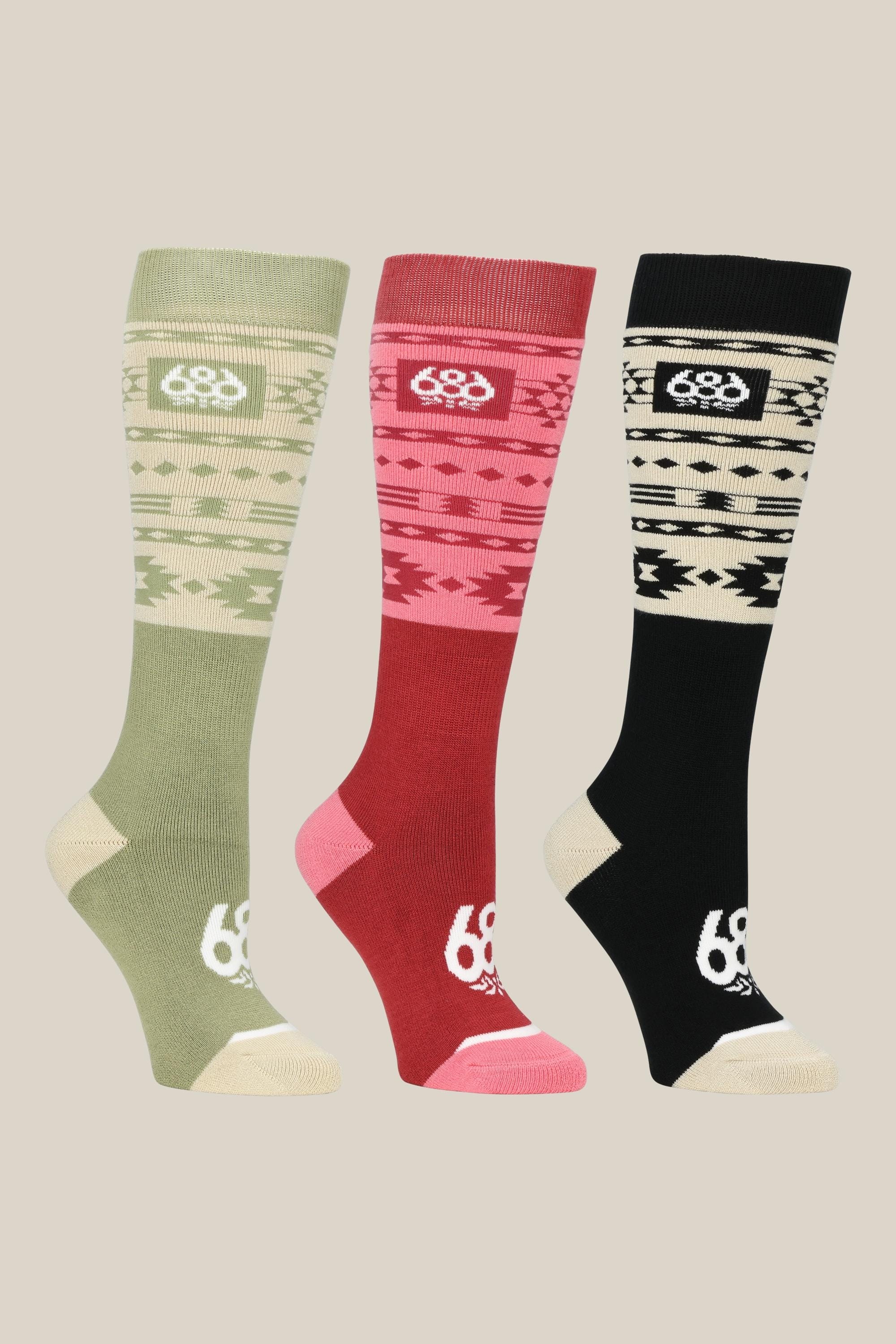 The 686 Womens Southwest Socks 3 Pack features green, red, and black acrylic socks with cream geometric patterns and logos, displayed side by side on a beige background.