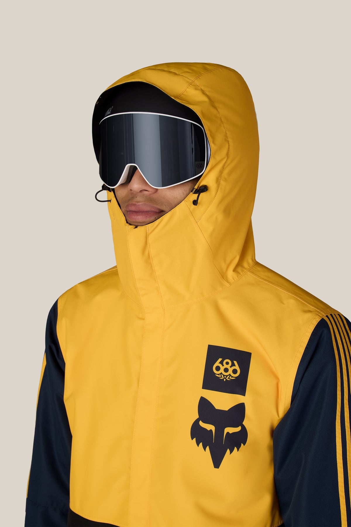 A person wearing a 686 Men’s Fox Racing Spec Insulated Jacket with a hood and ski goggles.