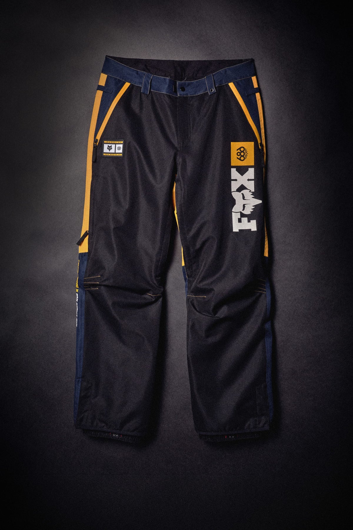 686 Men’s Fox Racing Spec Shell Pant in waterproof polyester with yellow and navy accents and leg logos.