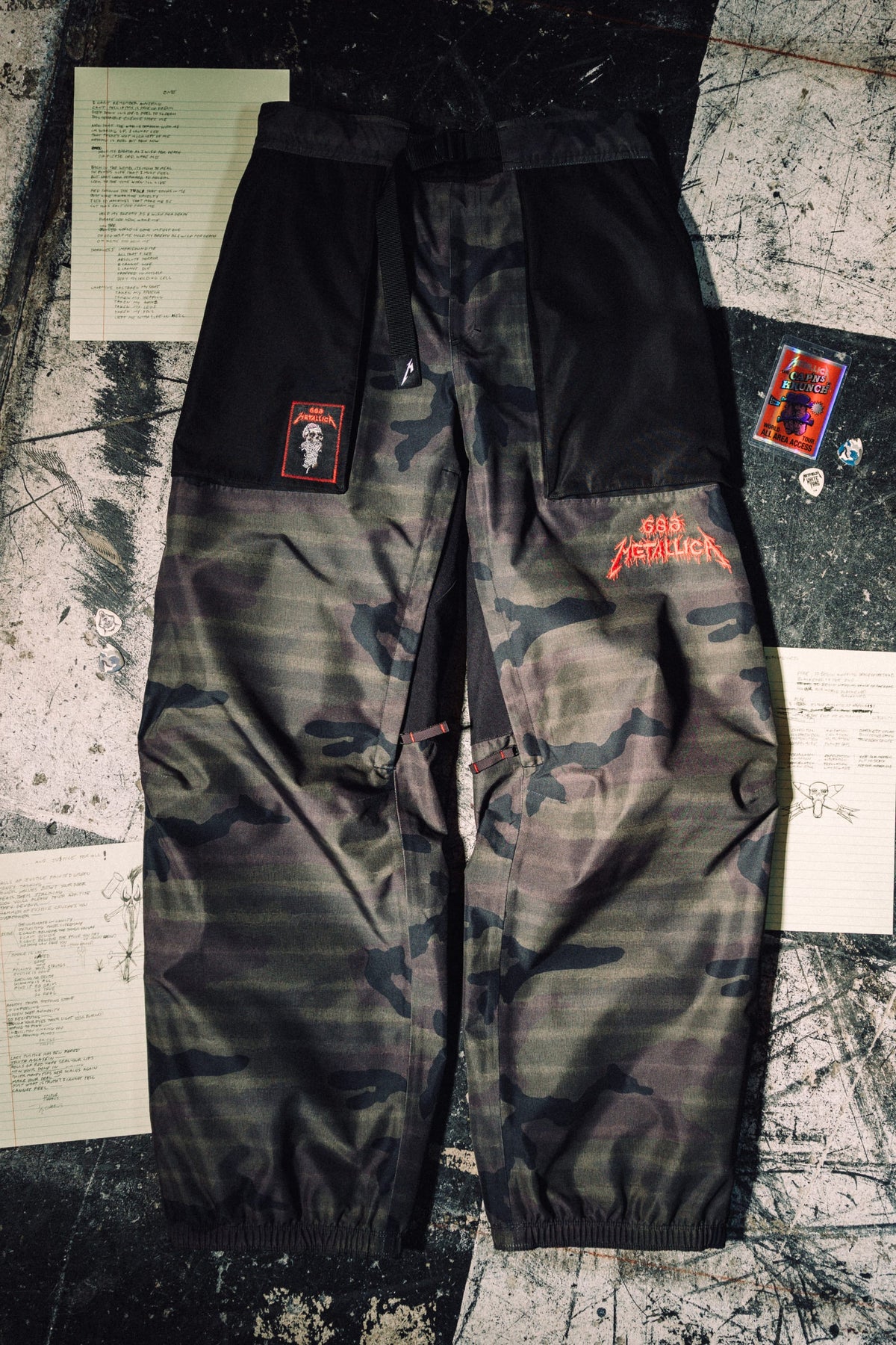 686 Men’s Metallica One Shell Pant in camo-print waterproof polyester with a Metallica logo on the thigh, a skull patch on the hip, and an integrated belt.