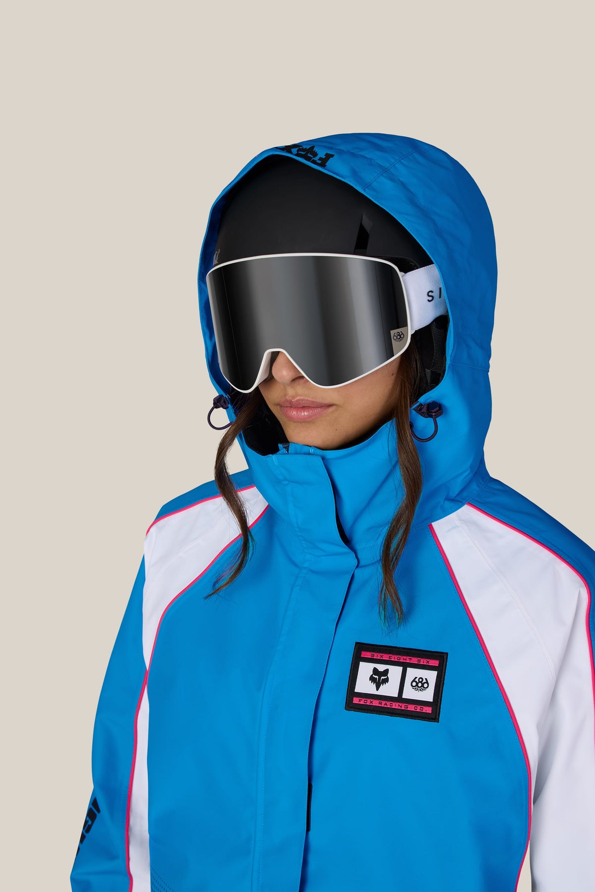 A person wearing a 686 Women’s Fox Racing 97 Shell Jacket, a black helmet, and 686 ski goggles.